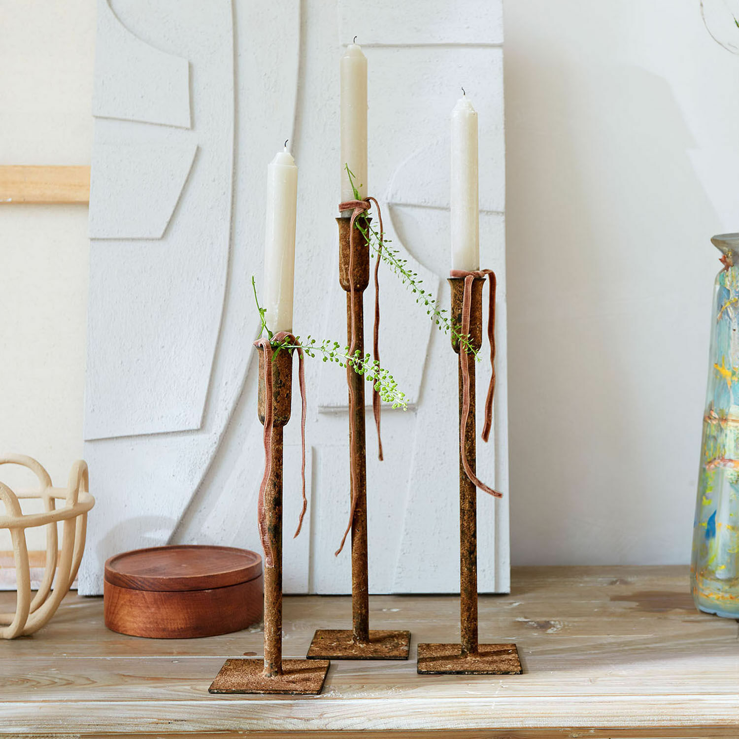 Lot de 3 bougeoirs Viverto Trois bougeoirs en métal rouillé avec bougies blanches et décorations végétales sur une table en bois