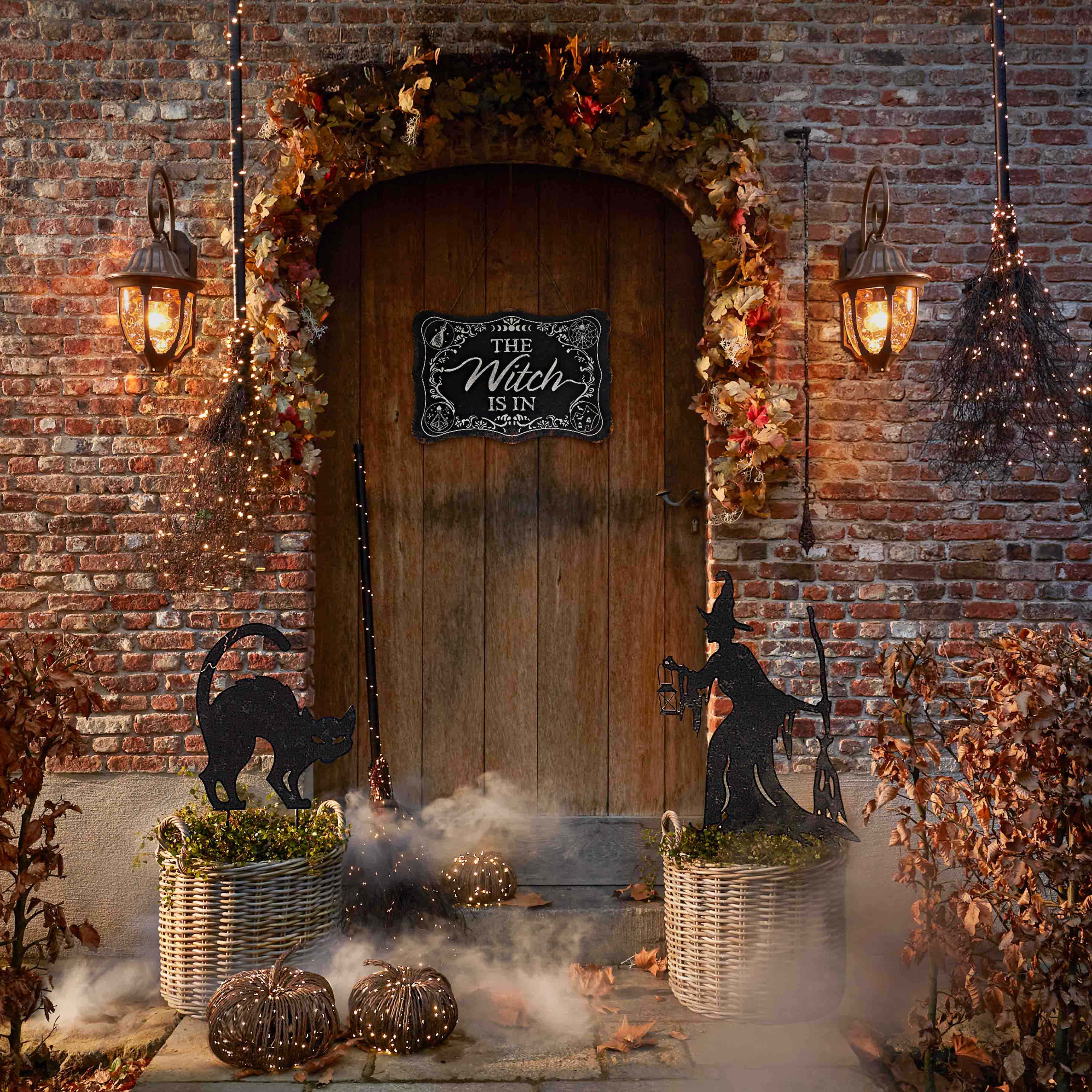 Décoration d'Halloween avec chat noir, sorcière et lanternes devant une porte en bois et mur en briques