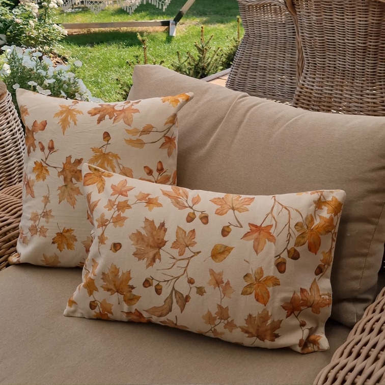 Coussins décoratifs en coton beige avec imprimé feuilles d'automne et glands sur canapé de jardin en osier