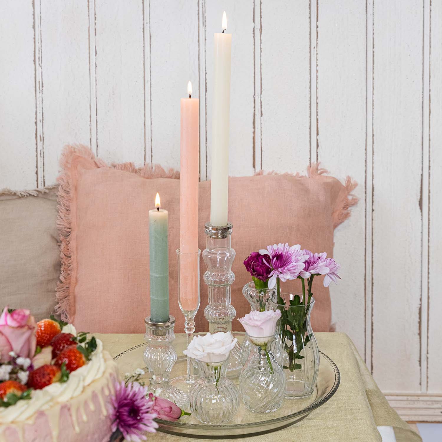 Bougies pastel et petits vases en verre avec fleurs sur un plateau en verre posé sur une table
