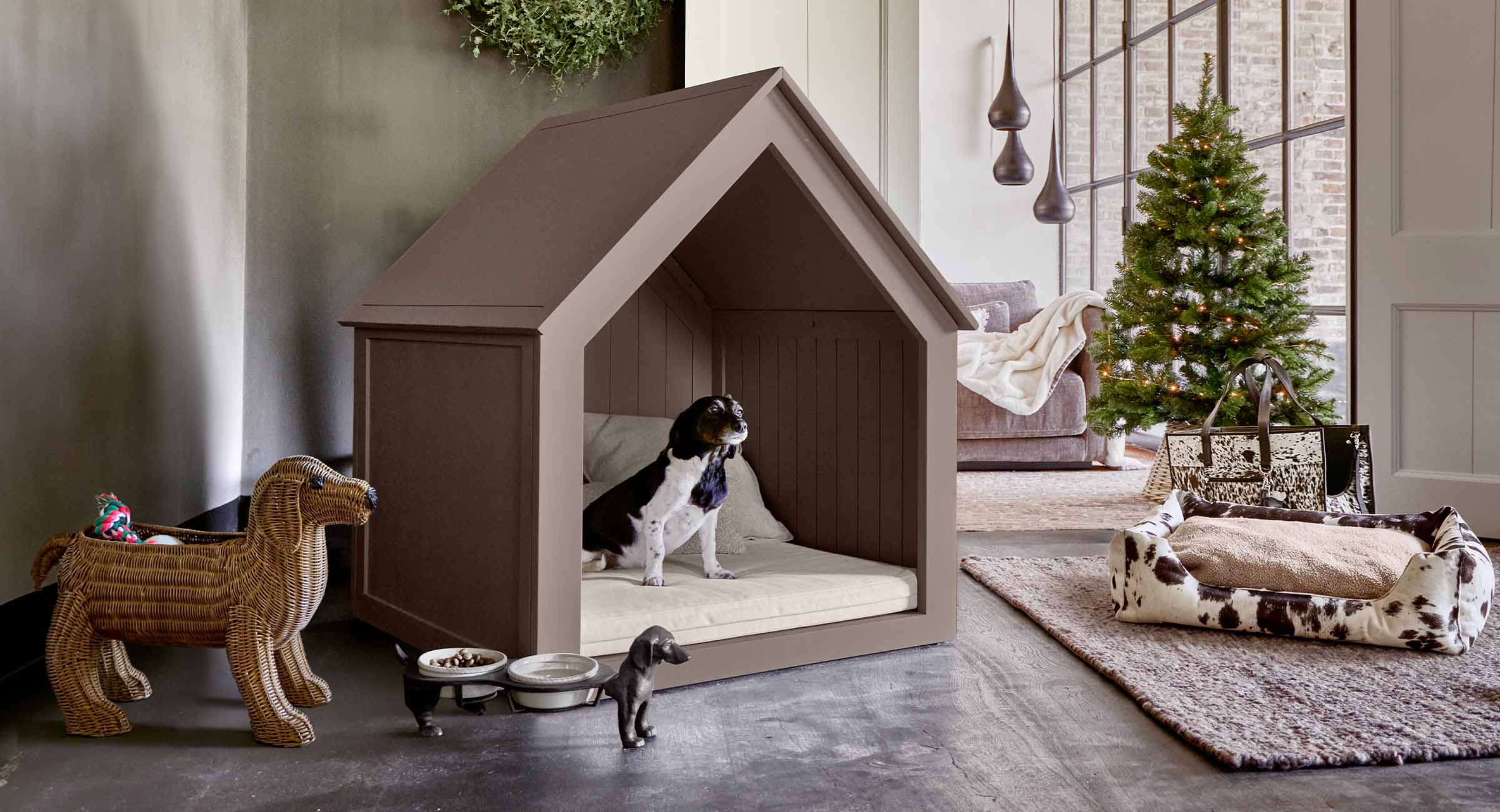 Maison pour chien en bois marron avec coussin crème dans un salon moderne décoré d'un sapin et jouets
