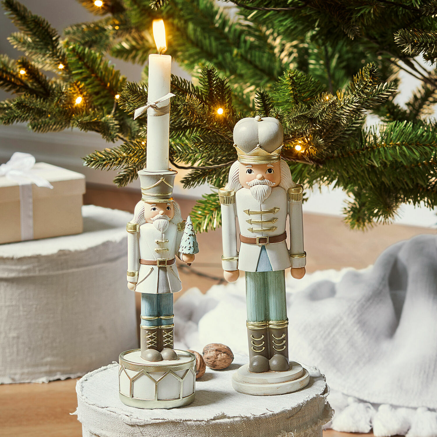 Casse-noisettes décoratif avec bougeoir Ellicott Figurines en bois de casse-noisette en blanc et vert devant un sapin de Noël décoré de lumières