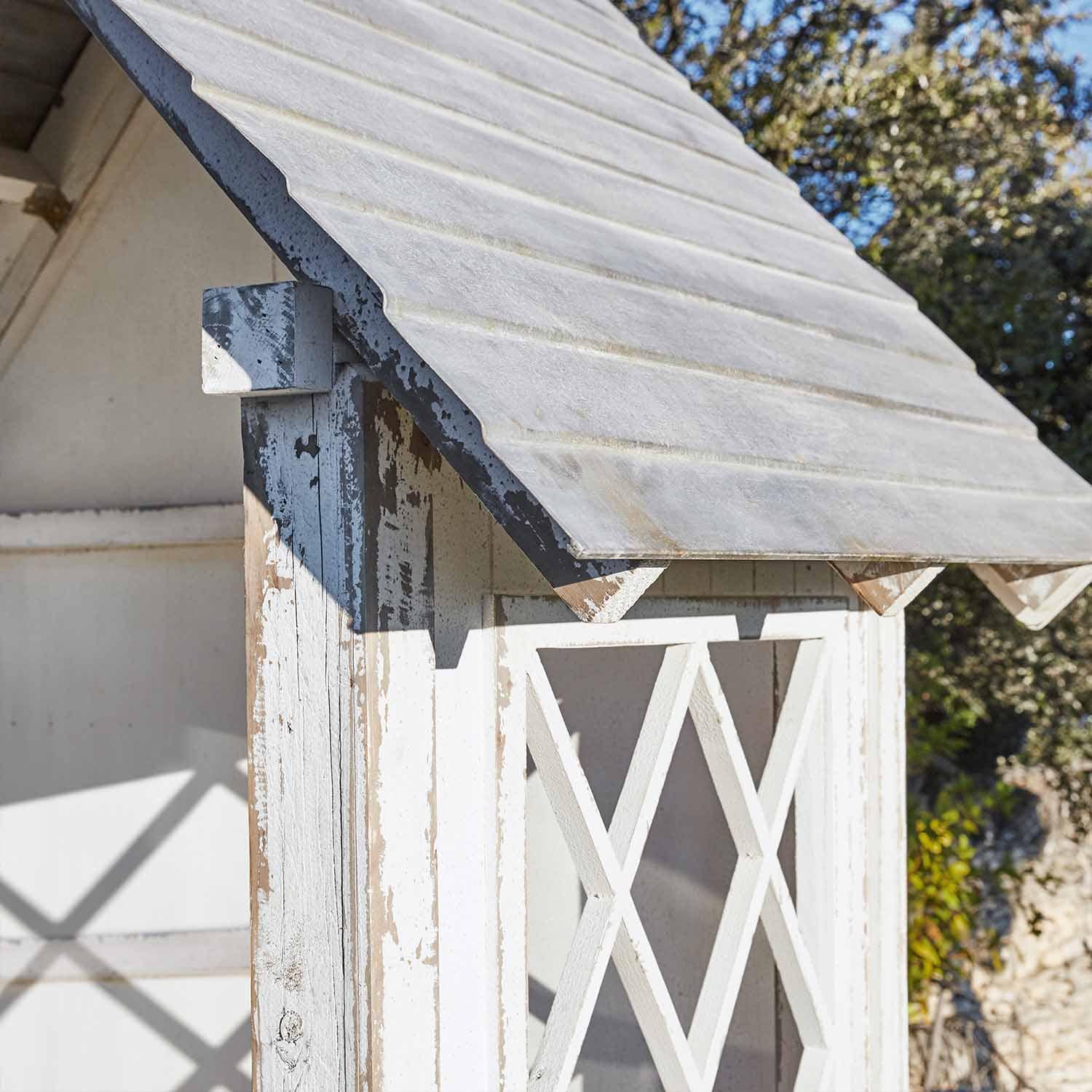 Petite maison de jardin en bois blanc vieilli avec toit incliné, décor extérieur rustique