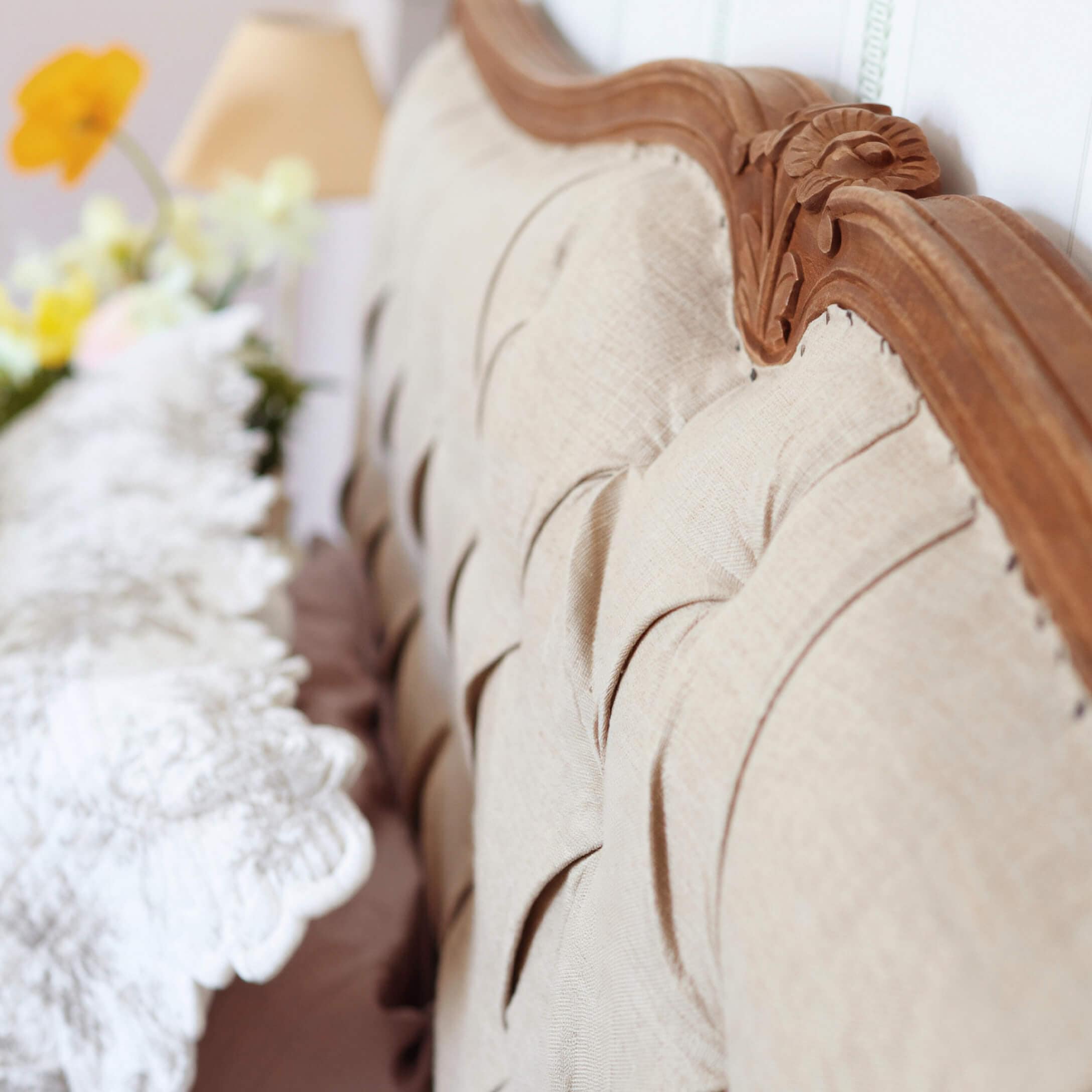 Dossier rembourré beige avec cadre en bois sculpté et coussin décoratif flou en arrière-plan