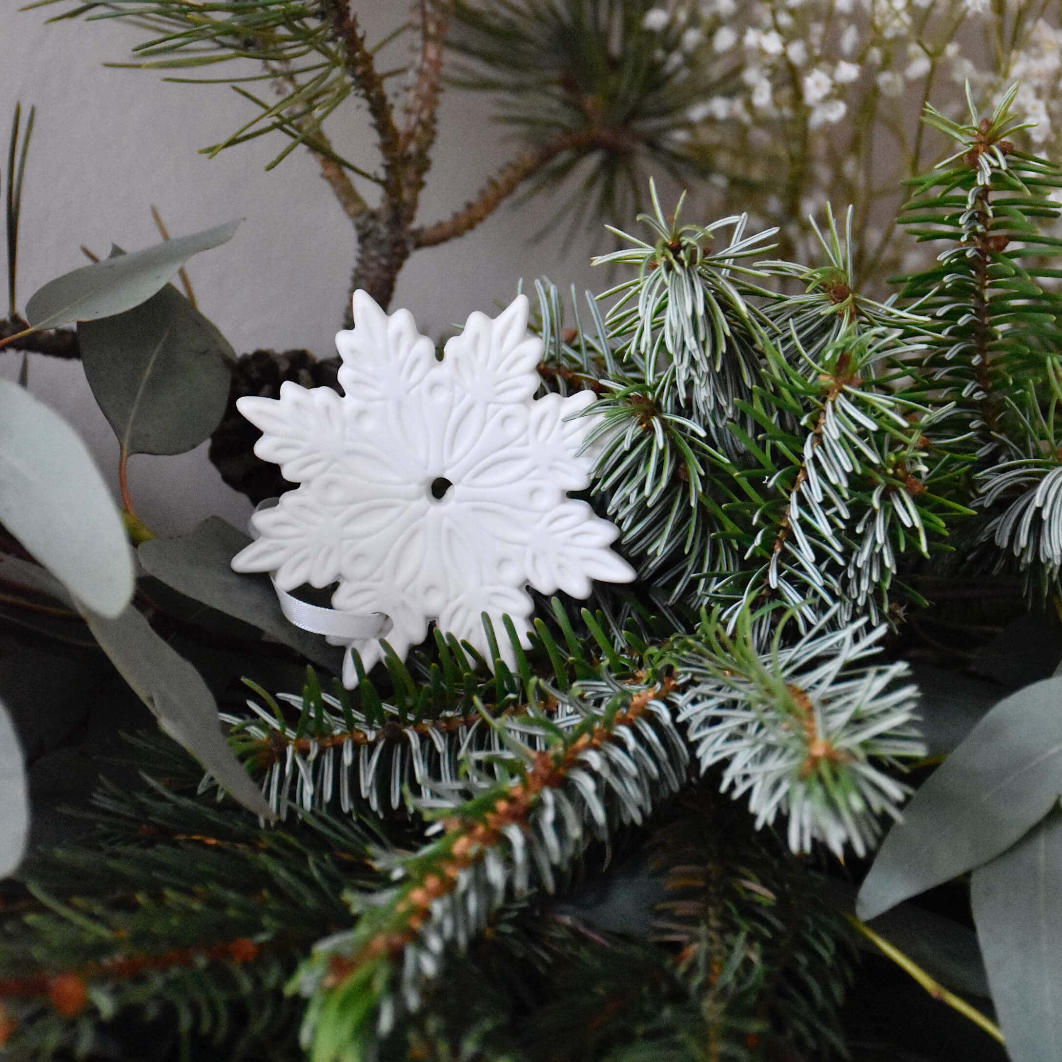 Décoration de Noël en céramique blanche en forme de flocon de neige sur branches de sapin vertes