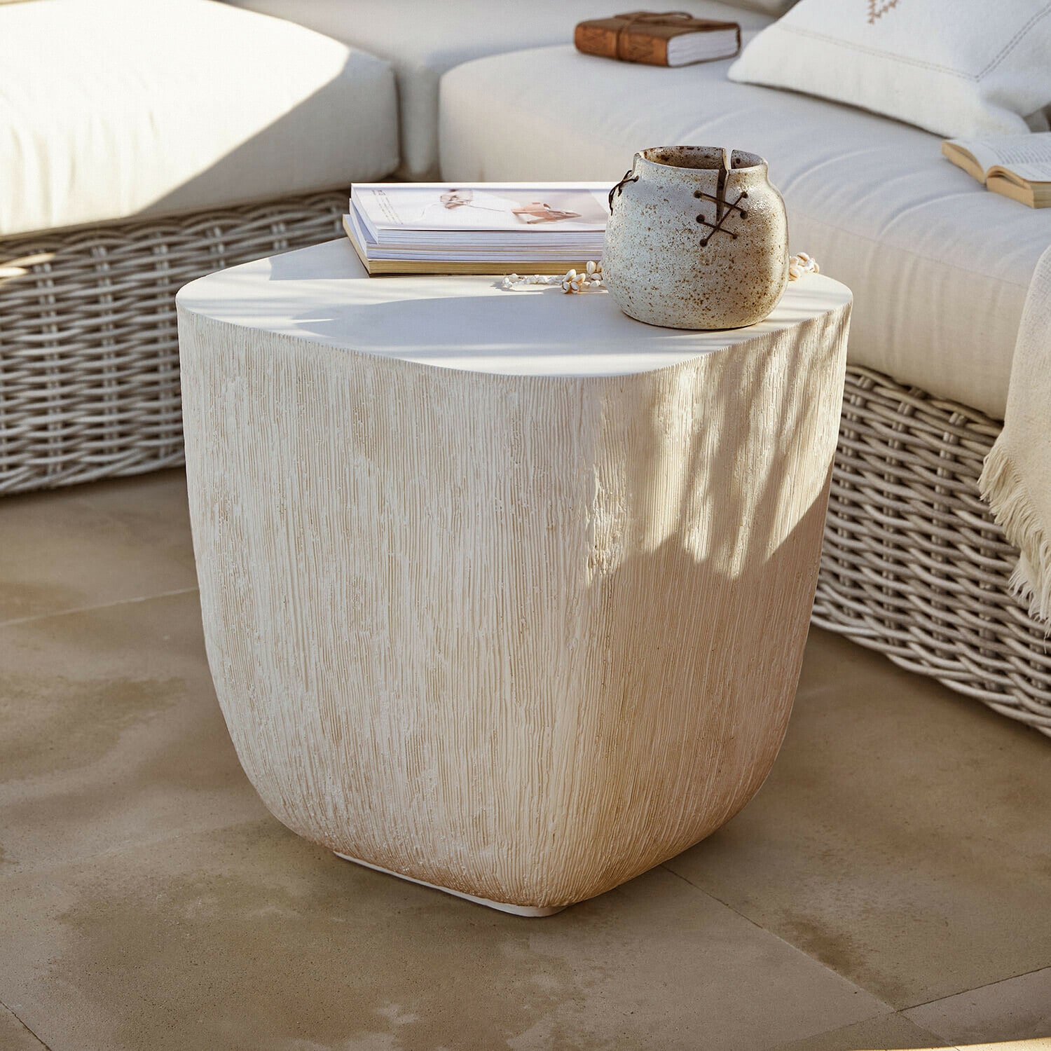Table d’appoint Nélomiane Table d'appoint beige texturée effet bois avec pot en céramique et livres sur terrasse avec canapé en osier