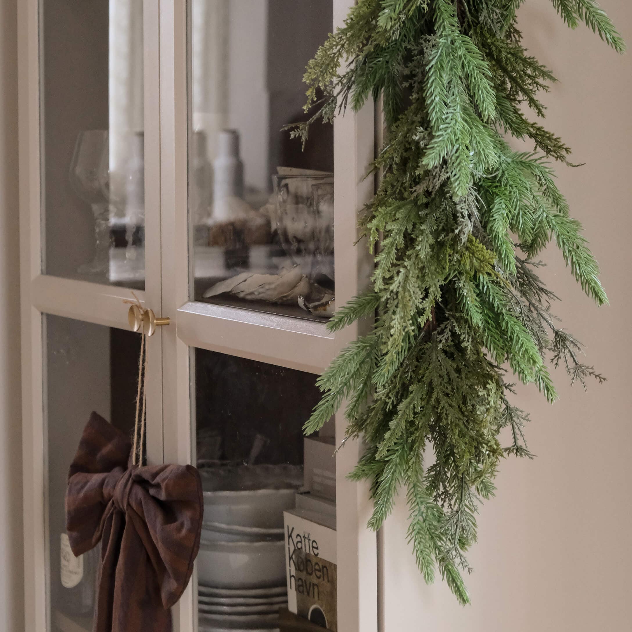 Guirlande verte décorative en branches suspendue sur une armoire claire avec portes vitrées style scandinave