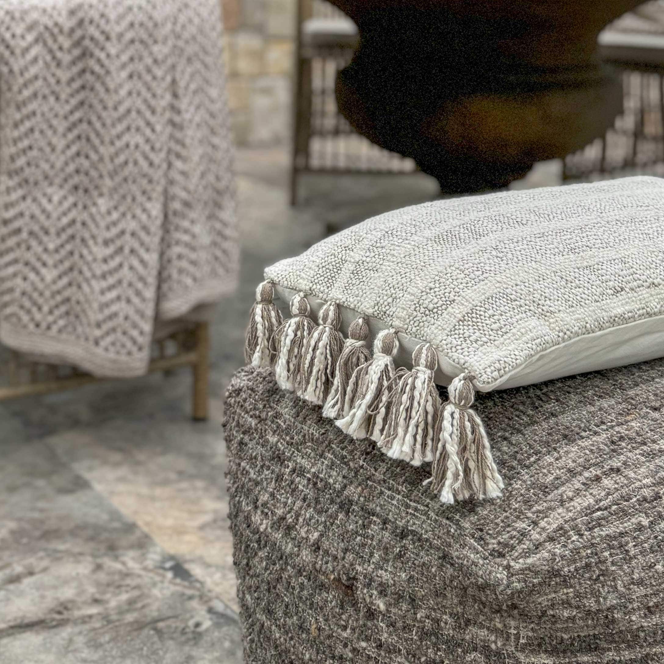 Coussin décoratif beige avec pompons sur pouf en laine grise, textile d'intérieur cosy