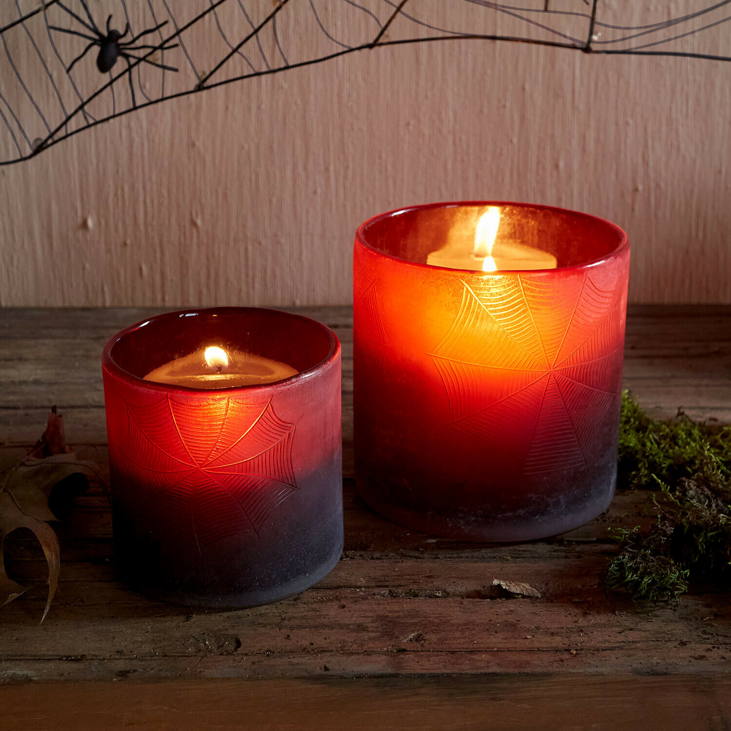 Lot de 2 photophores Brannora Deux photophores en verre rouge avec motif toile d'araignée, bougies allumées sur table en bois