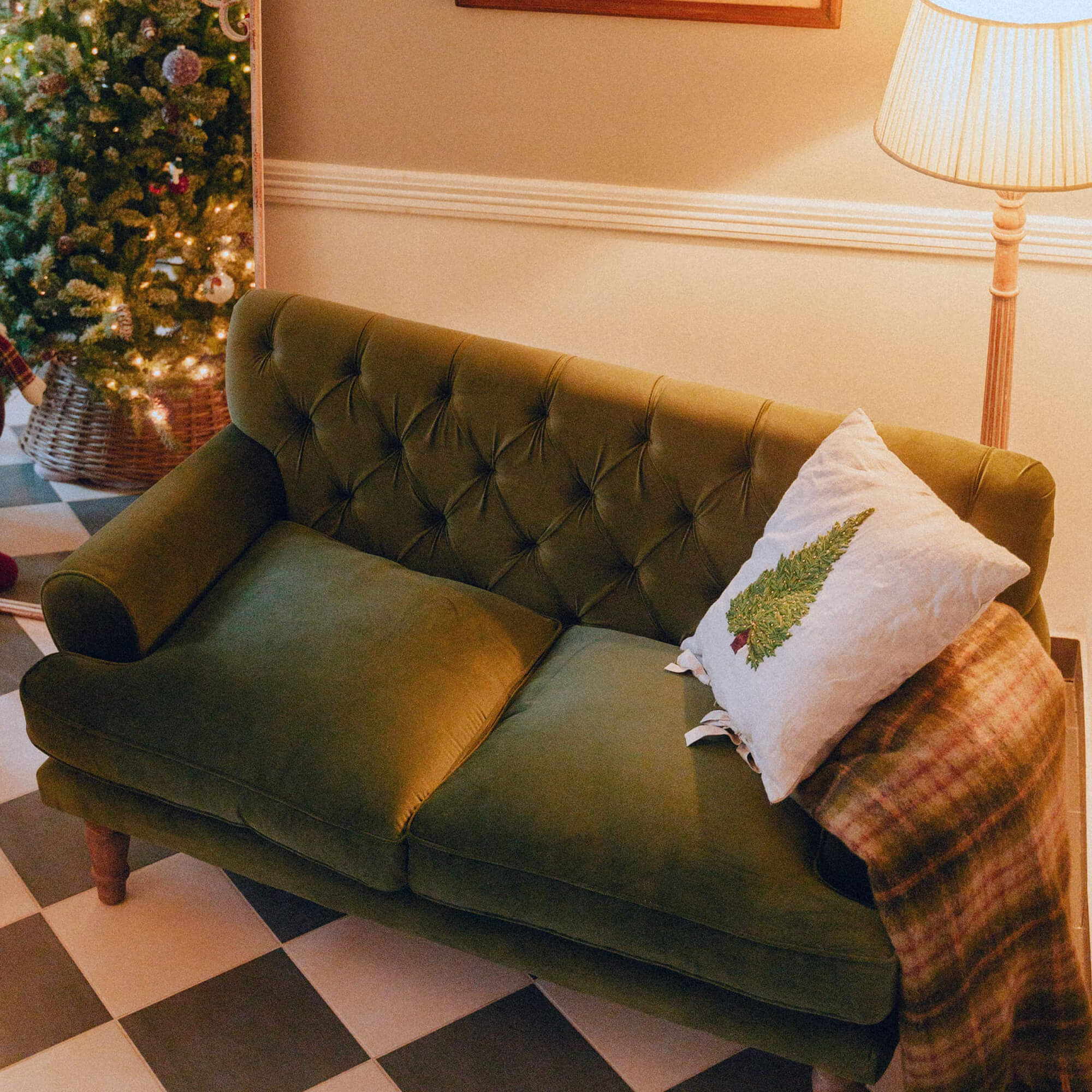 Canapé vert en velours avec dossier capitonné, coussin blanc sapin et plaid chaud dans un salon.