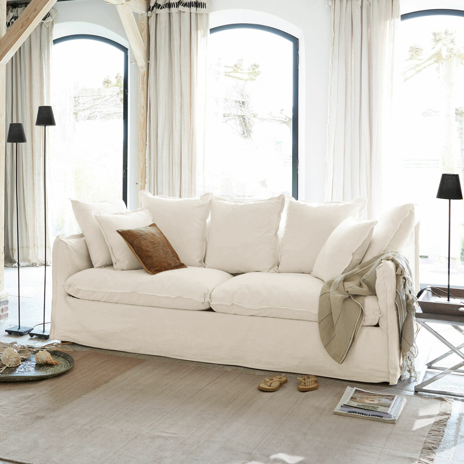 Canapé Tienen Canapé blanc avec coussins moelleux et coussin décoratif marron dans un salon lumineux aux grandes fenêtres