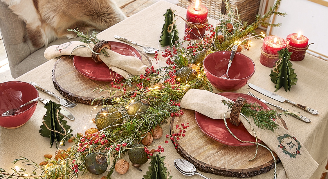 Table de Noël décorée avec assiettes rouges en céramique, décorations naturelles et bougies allumées