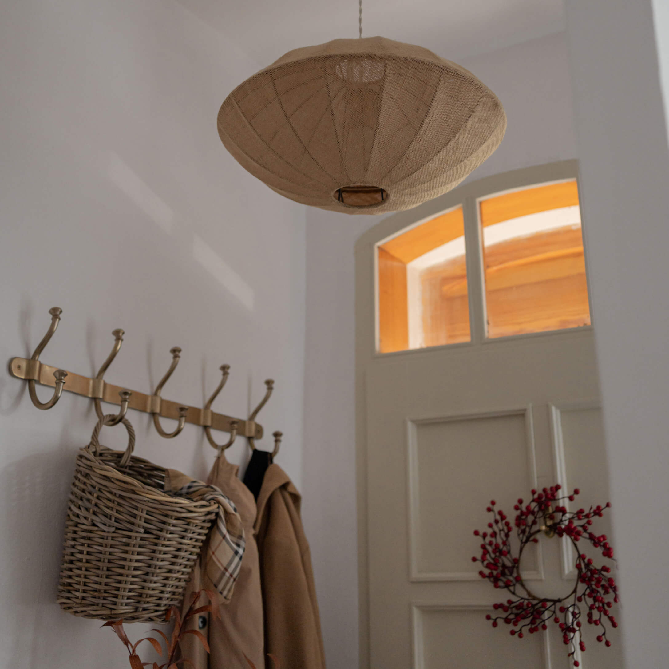 Suspension beige en tissu en forme de large abat-jour dans une entrée avec porte blanche et patères en métal doré