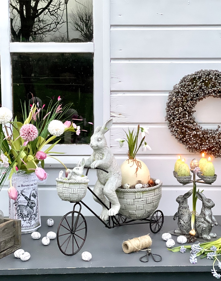 Décoration de Pâques avec lapins gris en métal et céramique sur table avec fleurs et bougies