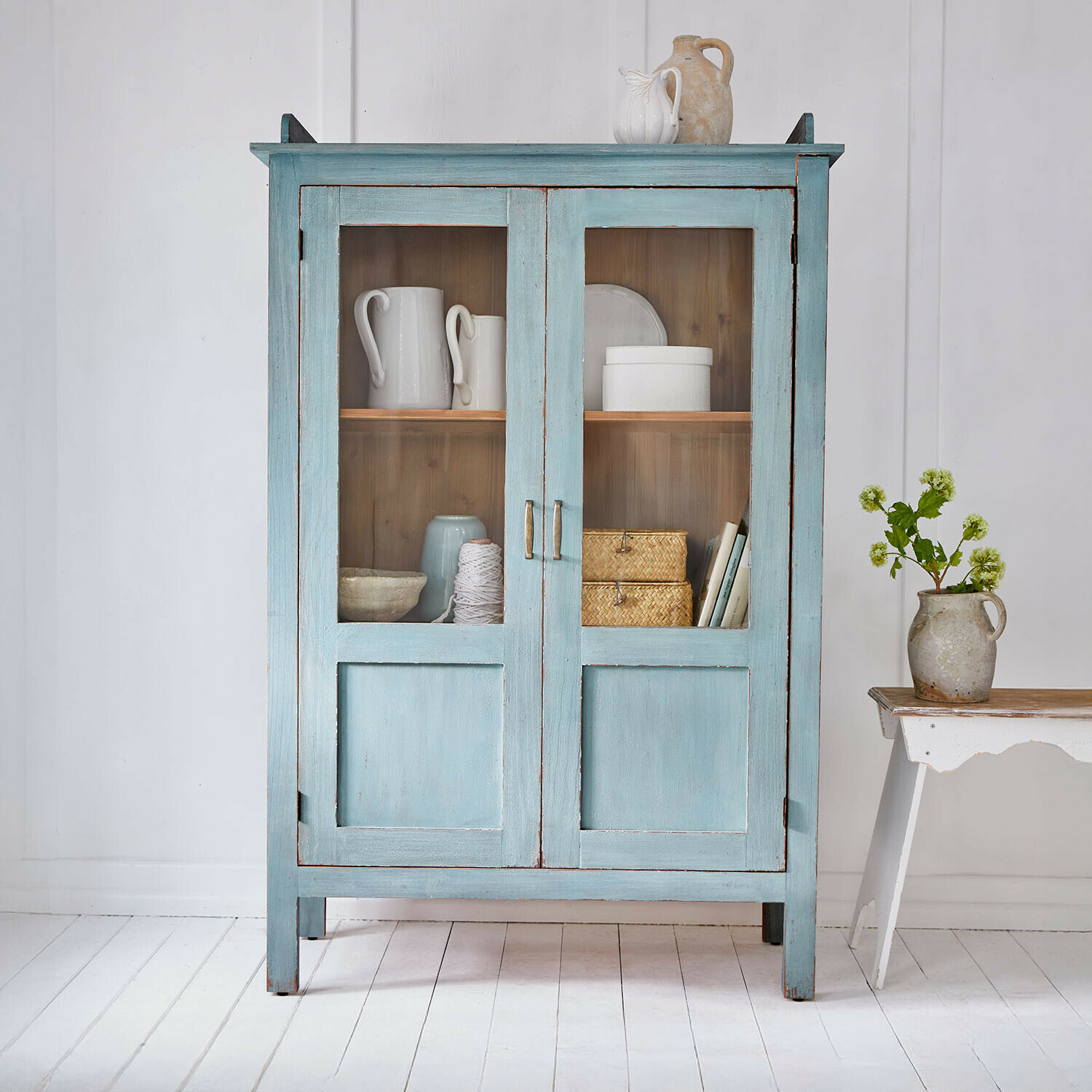 Vitrine Nouvellese Armoire en bois bleu avec portes vitrées et décorations en céramique style vintage dans une pièce claire