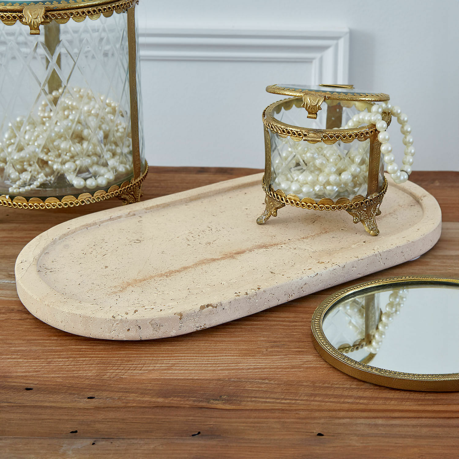 Coupelle Thalina Boîte en verre avec cadre en laiton et perles sur plateau en pierre beige sur table en bois