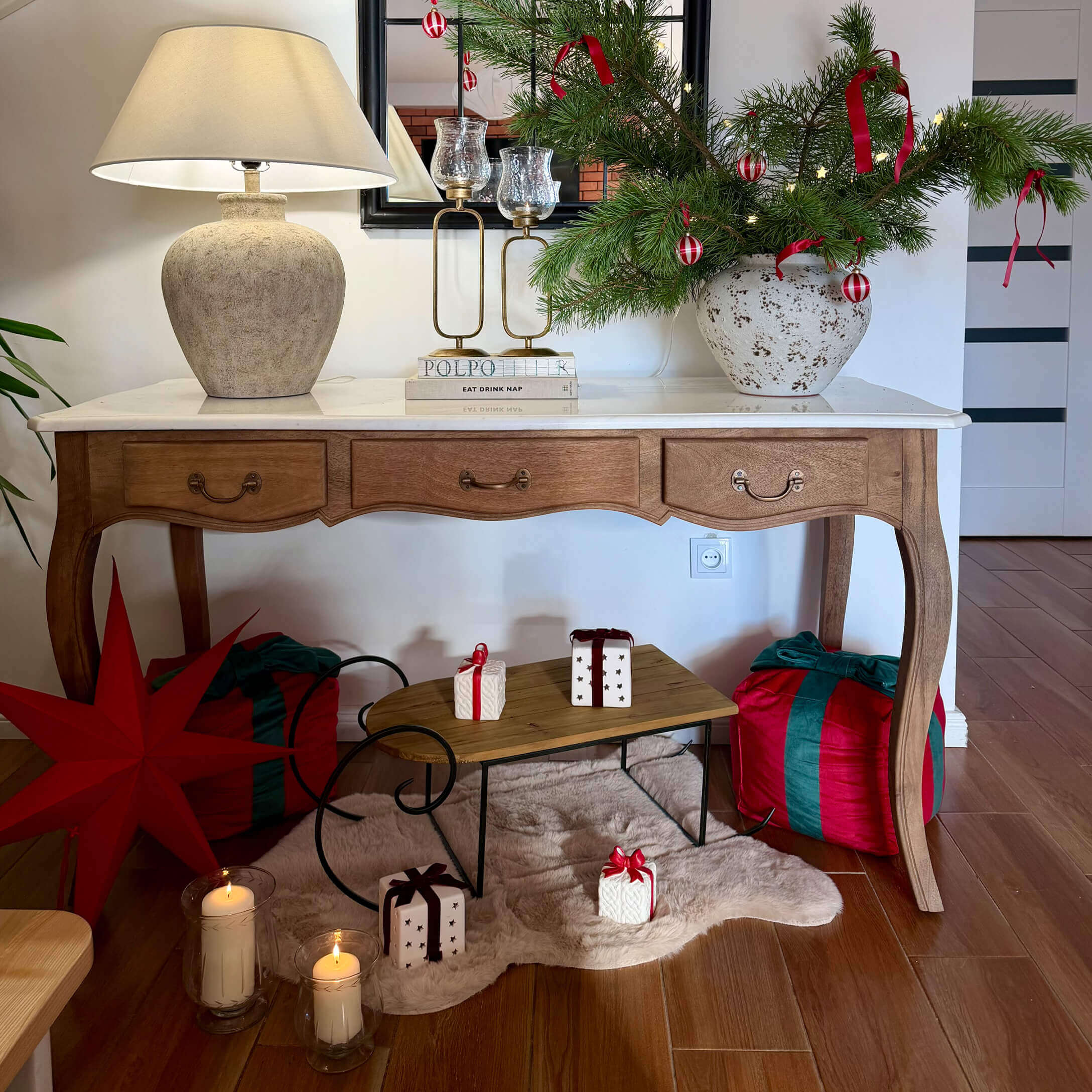 Table en bois avec plateau blanc, lampe et décoration de Noël avec branches vertes et rubans rouges