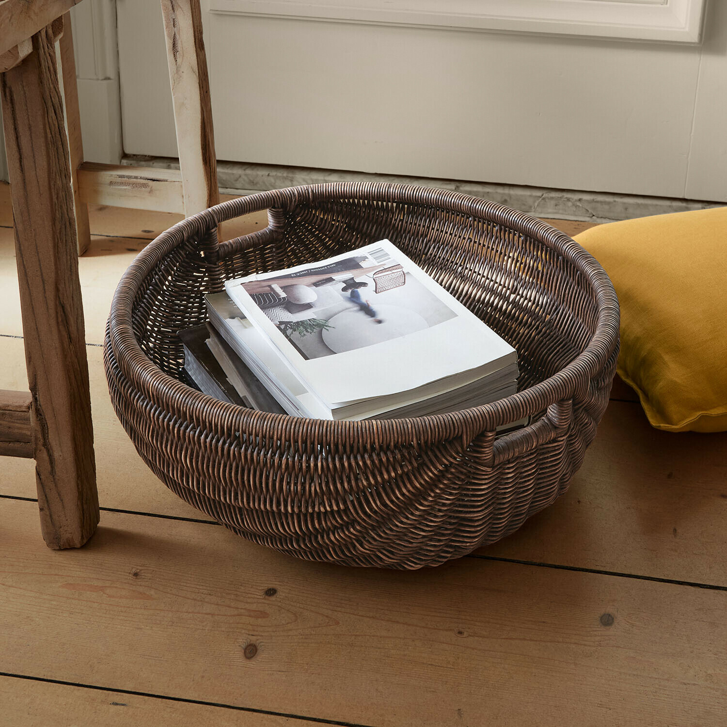 Panier Veltris Panier rond en rotin foncé avec poignées, contenant des livres sur un sol en bois clair