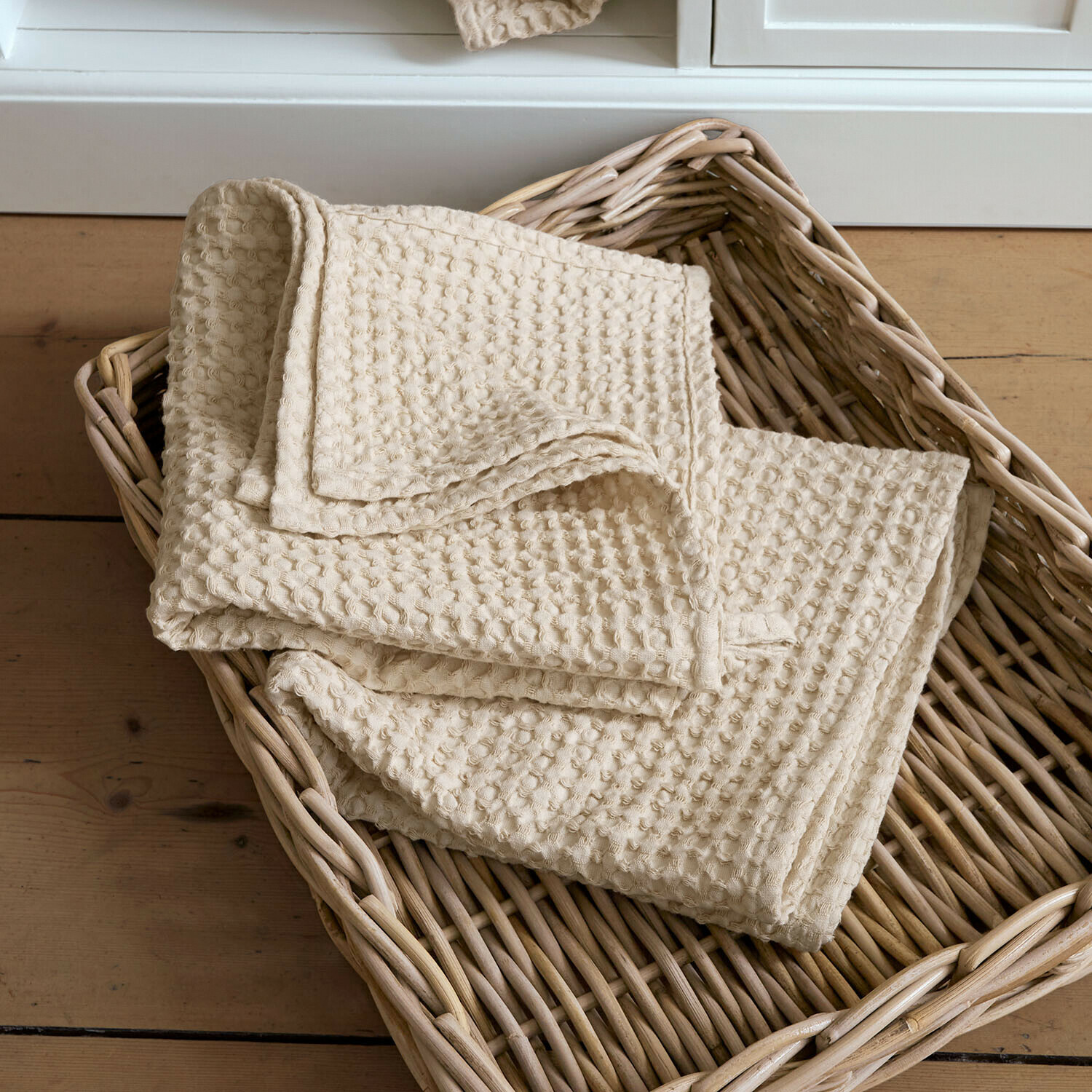 Lot de 2 serviettes Maralei Serviette beige en coton gaufré posée dans un panier en osier sur un sol en bois