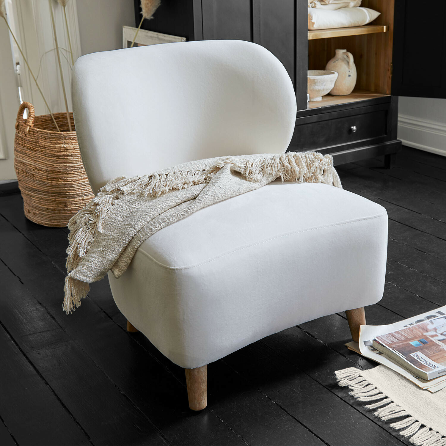 Fauteuil blanc rembourré avec pieds en bois et plaid beige sur un sol noir dans un salon moderne