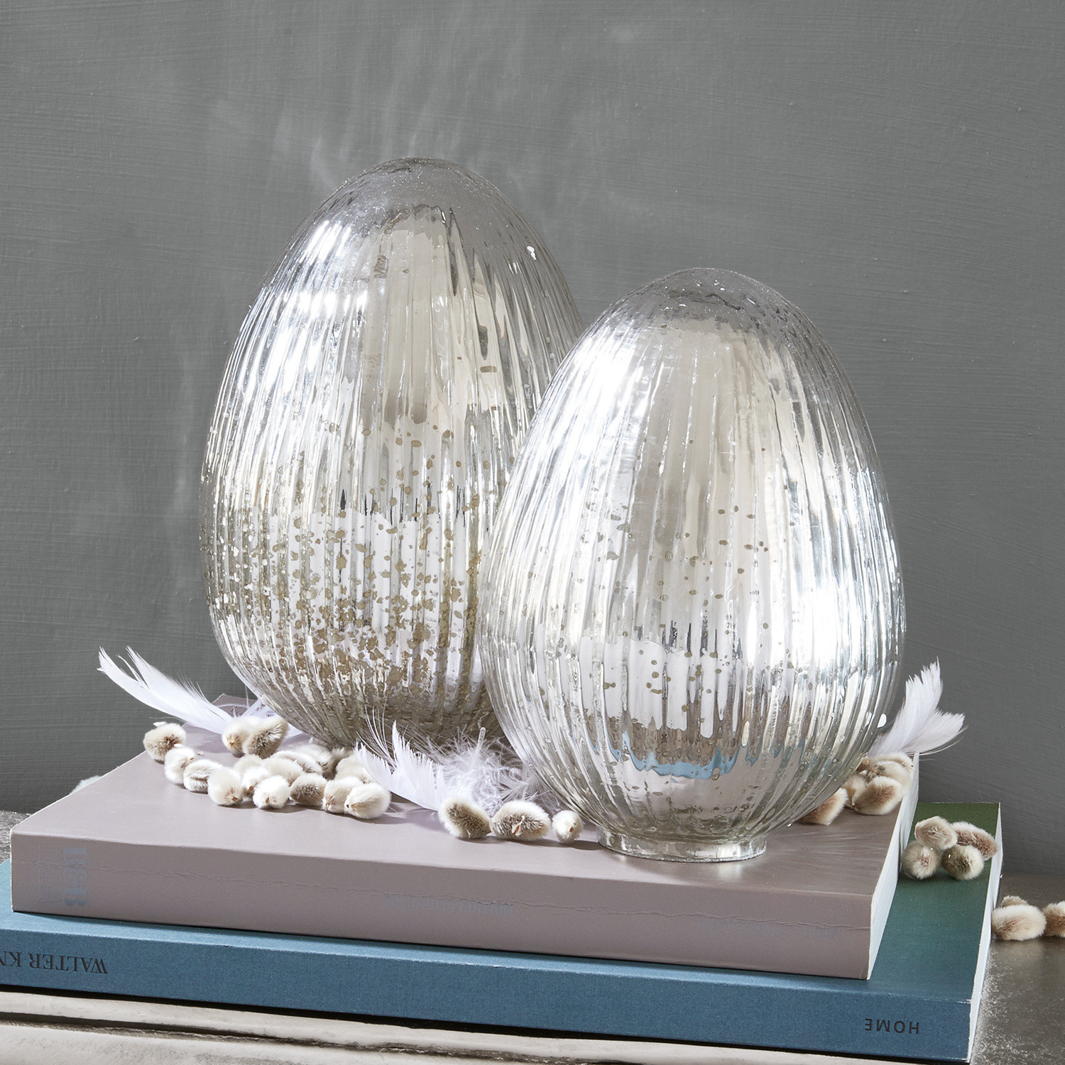 Lot de 2 œufs de Pâques Duvera Deux bougeoirs décoratifs en verre argenté posés sur des livres, ornés de plumes et chatons