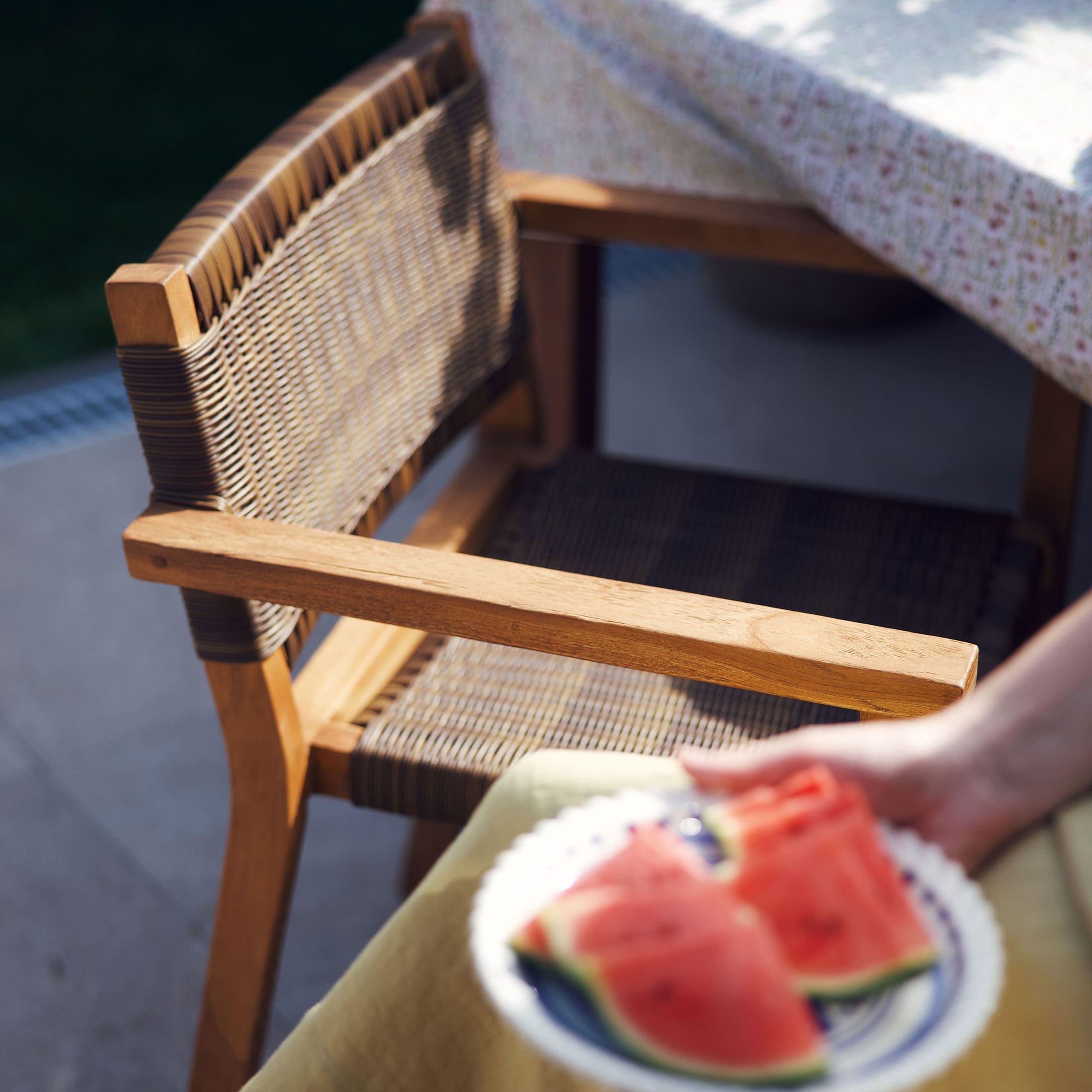 Chaise de jardin en bois et rotin naturel près d'une table avec nappe fleurie