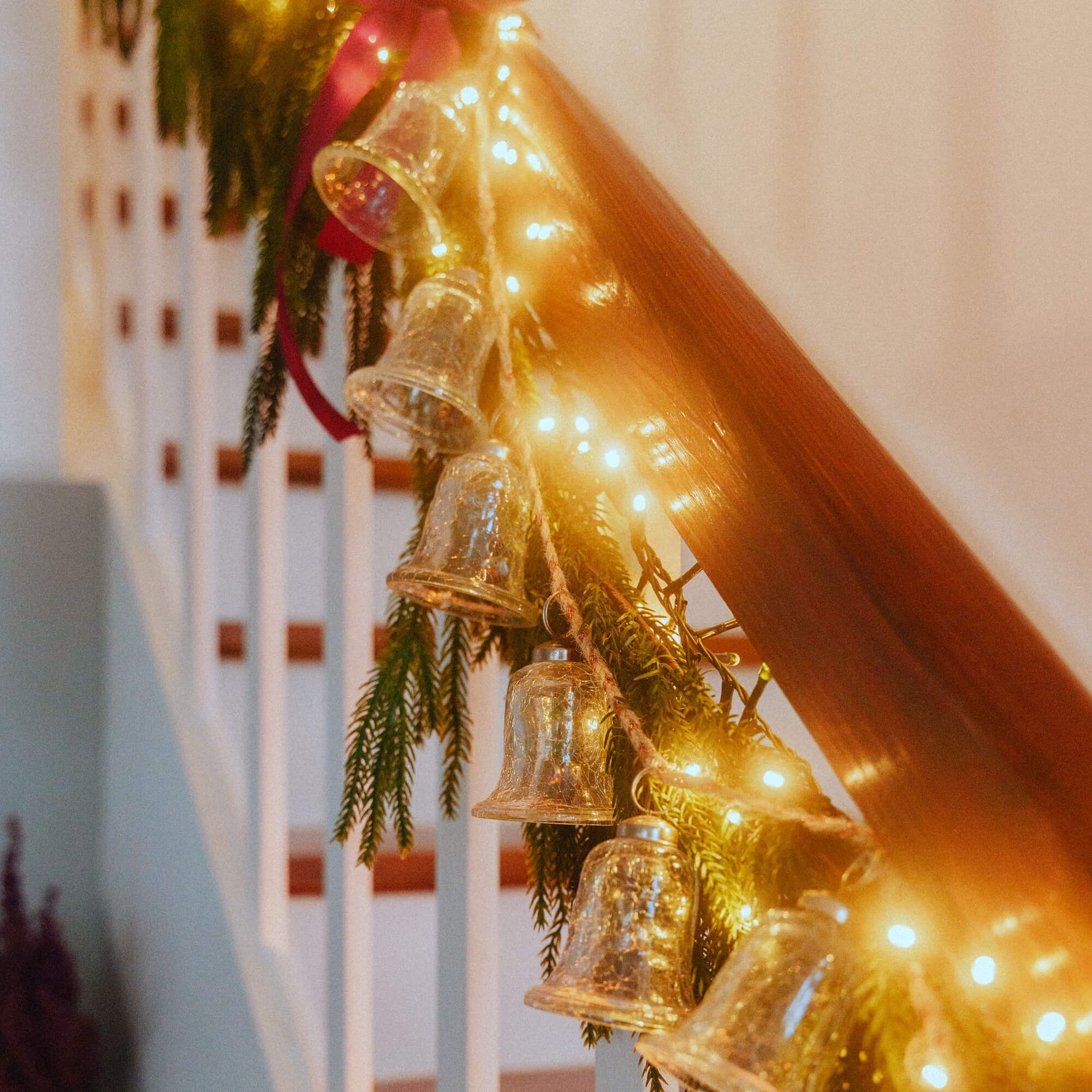 Clochettes en verre et guirlande lumineuse LED sur rampe en bois avec branches vertes, décoration festive