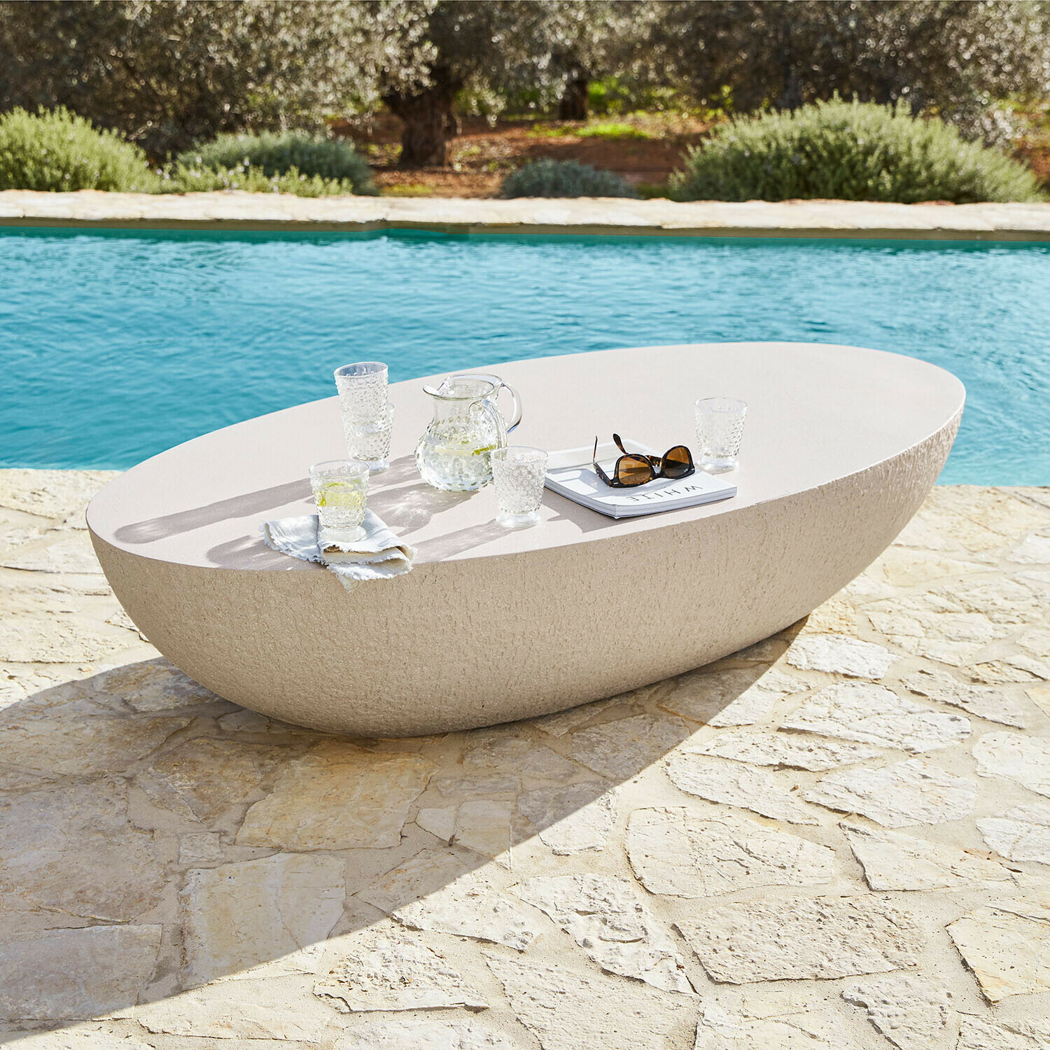Table ovale en pierre claire sur terrasse en pierre près de la piscine, mobilier extérieur moderne