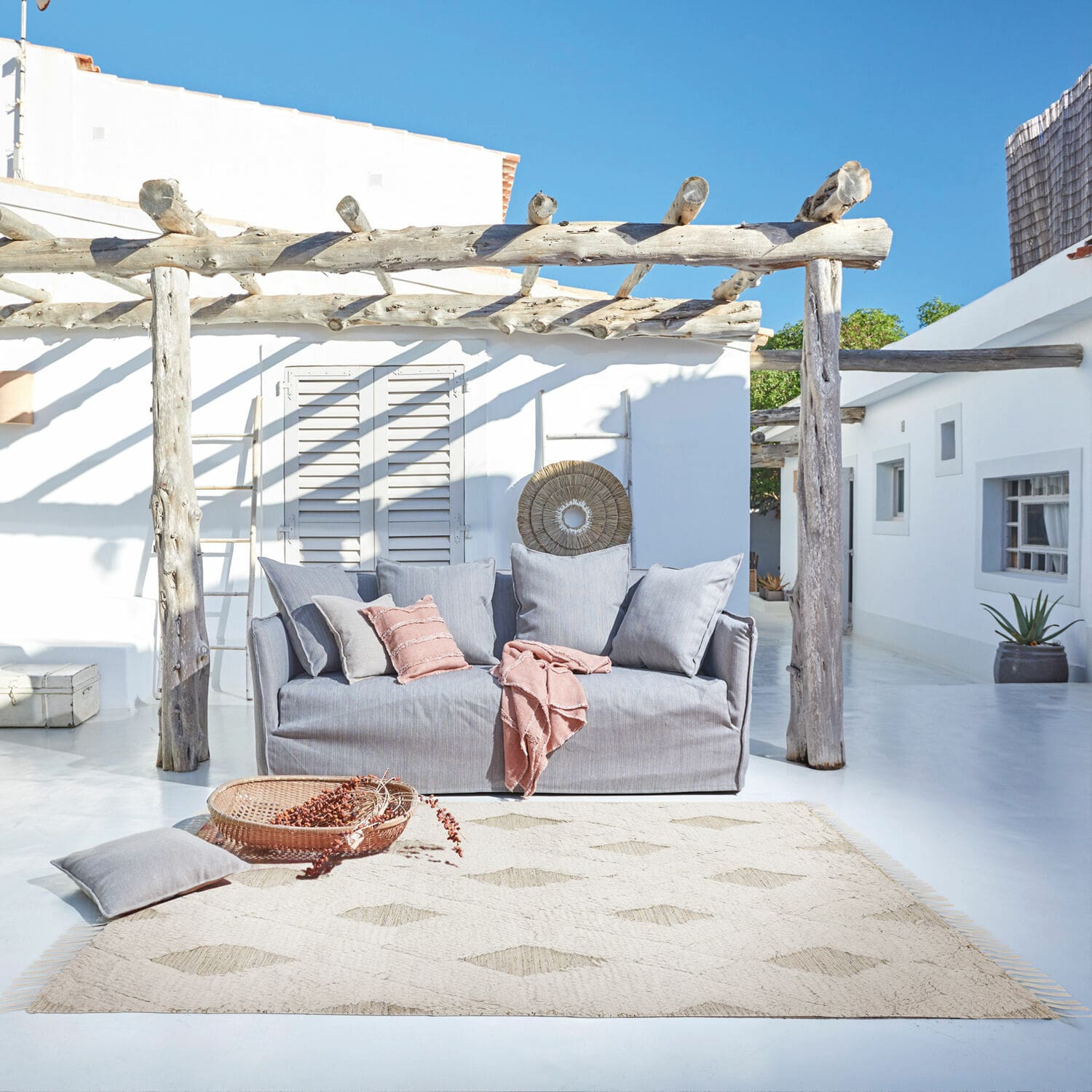 Tapis d’intérieur et d’extérieur Meagan Canapé gris en tissu sur terrasse avec tapis naturel et coussins roses pour détente extérieure