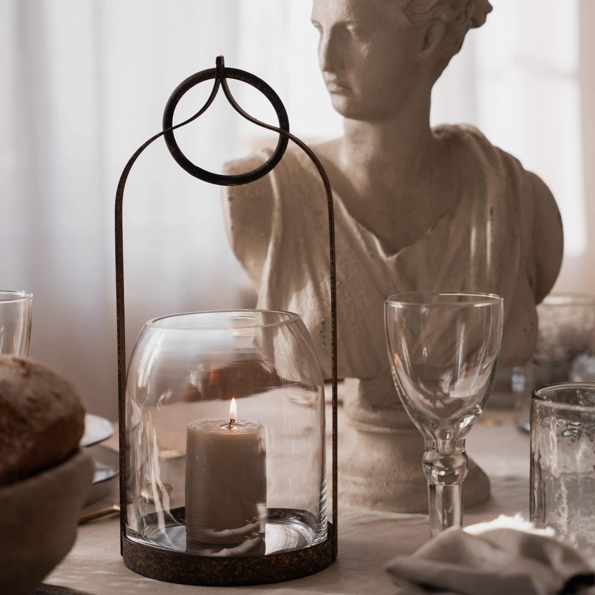 Lanterne en verre avec cadre métallique rouillé et bougie allumée sur table rustique avec statue décorative