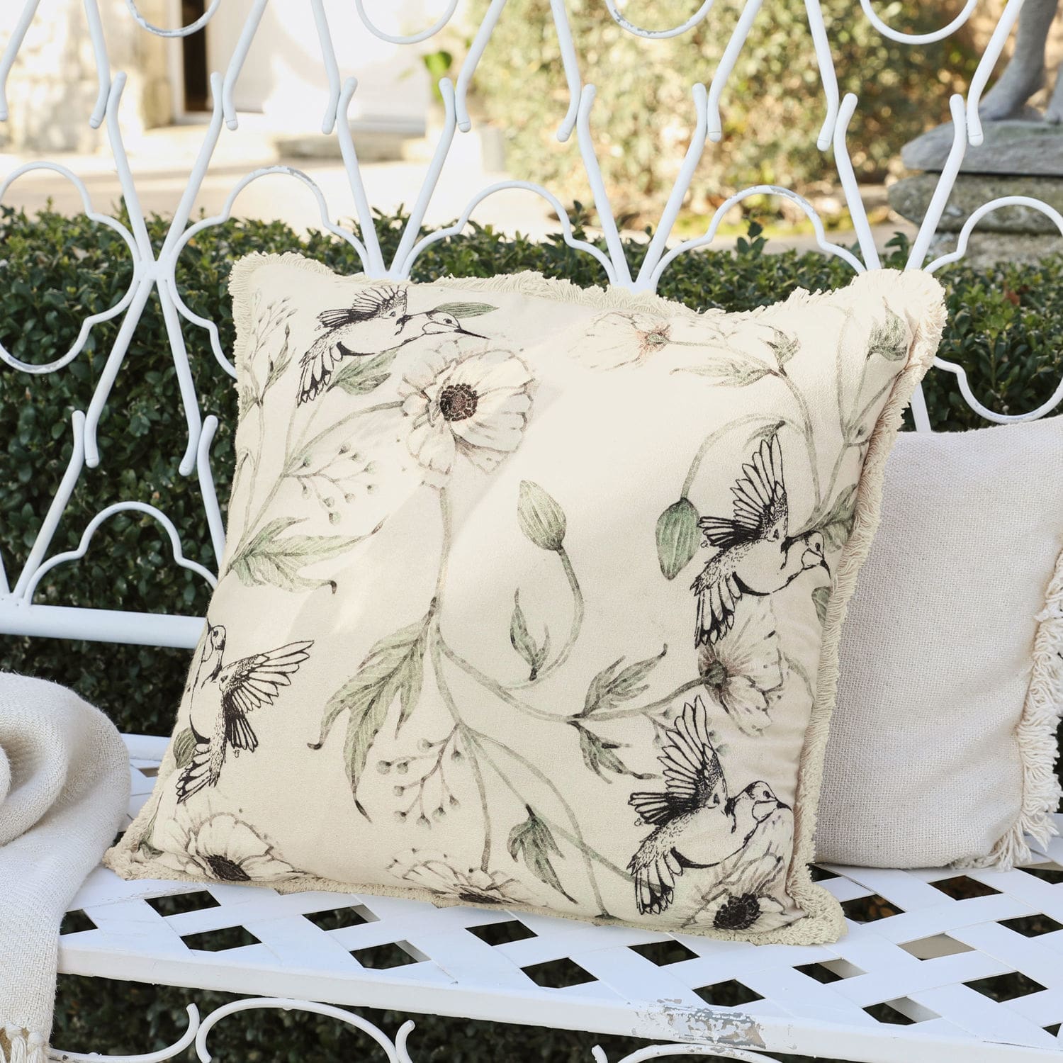 Housse de coussin Byrne Coussin beige décoratif avec motif d'oiseaux et fleurs sur banc en métal blanc dans un jardin