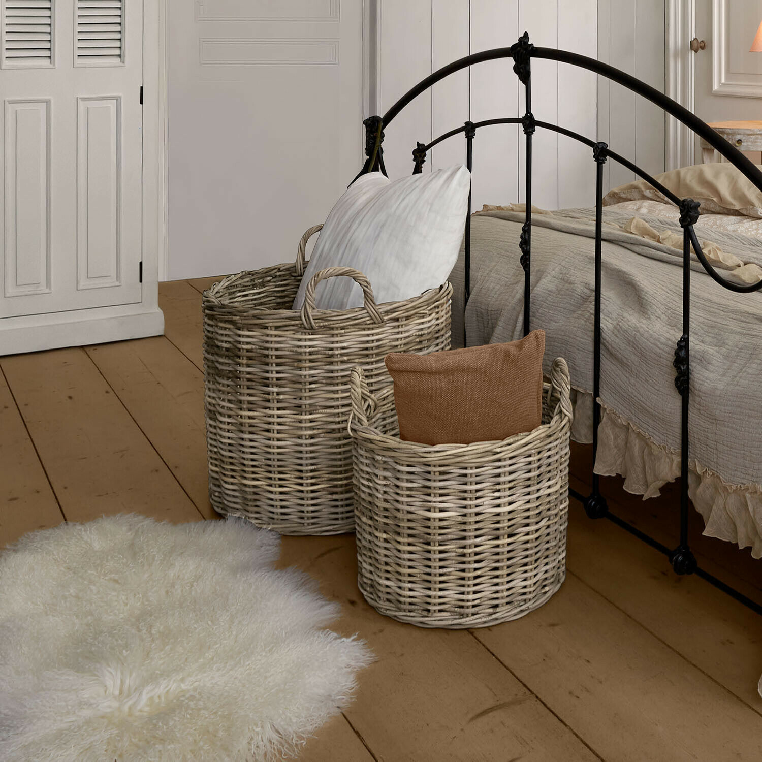 Lot de 2 paniers Alouenne Deux paniers en osier naturel avec coussins dans une chambre avec lit en métal et parquet en bois