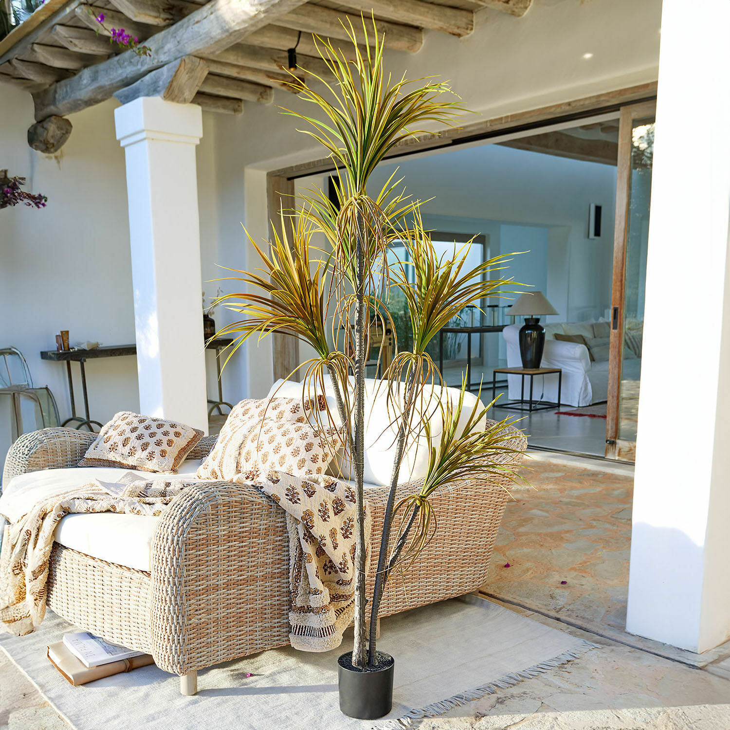 Plante décorative en pot Ancerac Plante artificielle en pot noir sur terrasse avec canapé en osier et couverture claire