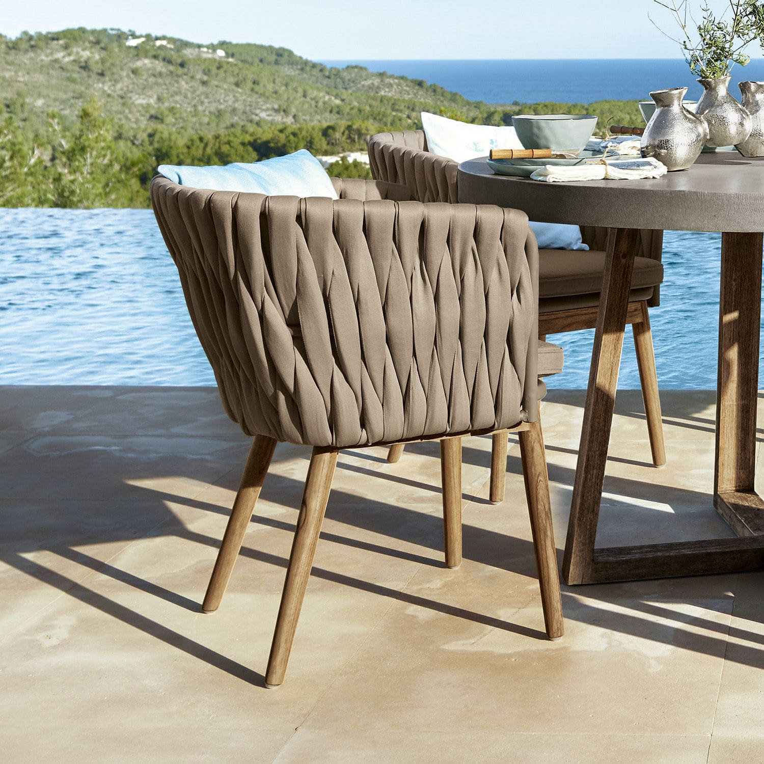 Chaise Uchon Chaise d'extérieur beige avec dossier tressé et pieds en bois sur terrasse avec vue sur la mer