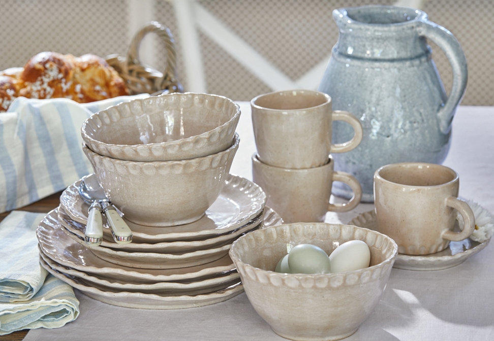 Service de vaisselle en céramique beige avec assiettes, bols et tasses sur une table rustique