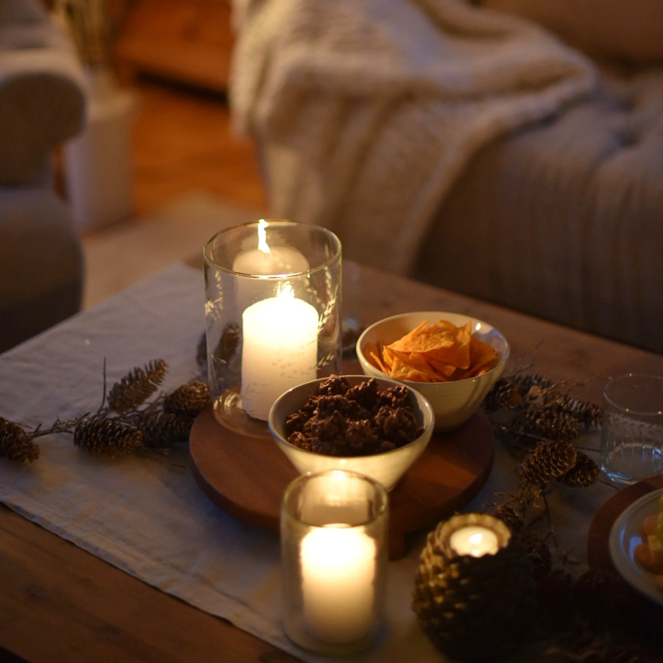 Bougies dans des photophores en verre et bols de snacks sur une table en bois dans un intérieur chaleureux