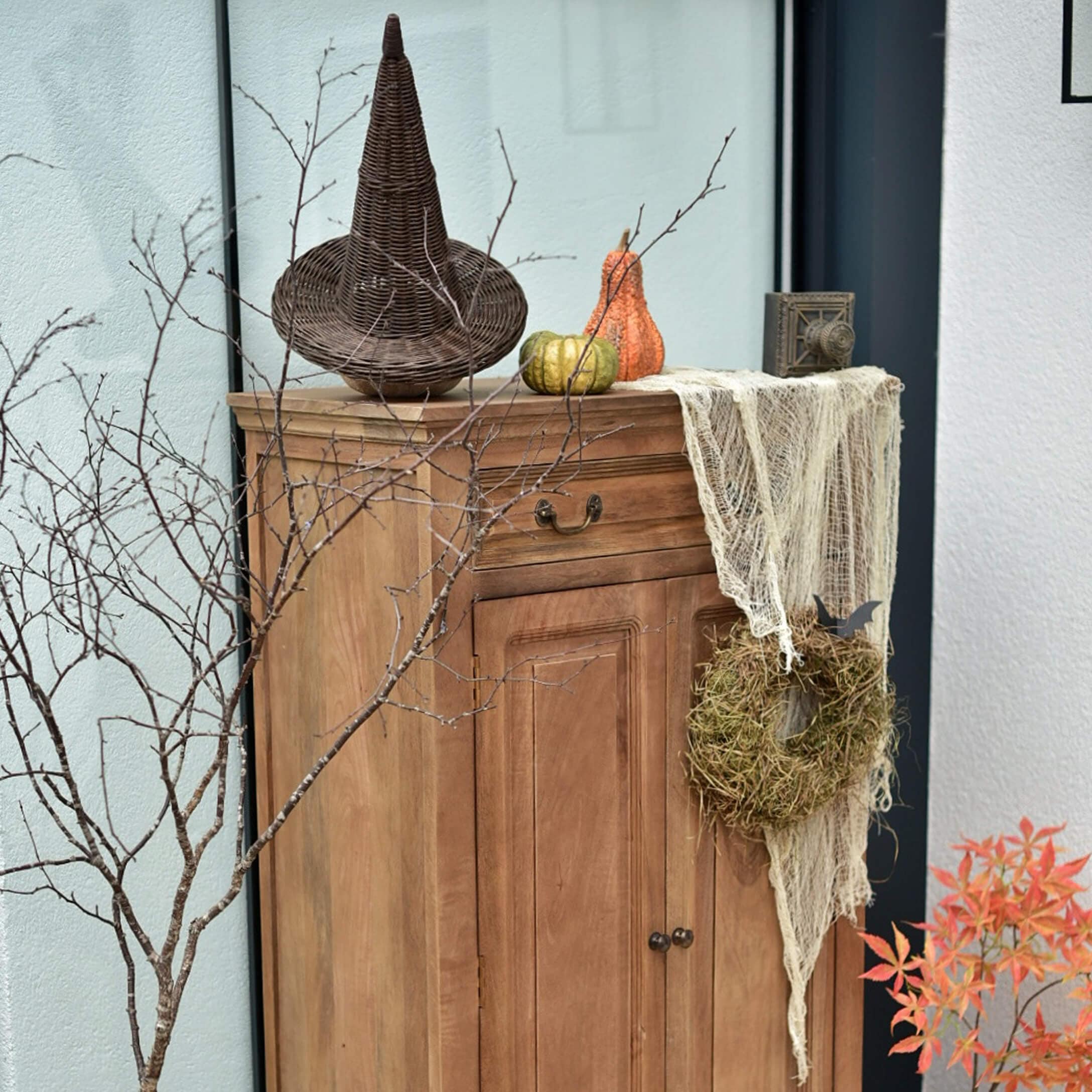 Armoire en bois avec décorations d'automne : chapeau en osier, citrouilles et couronne de mousse
