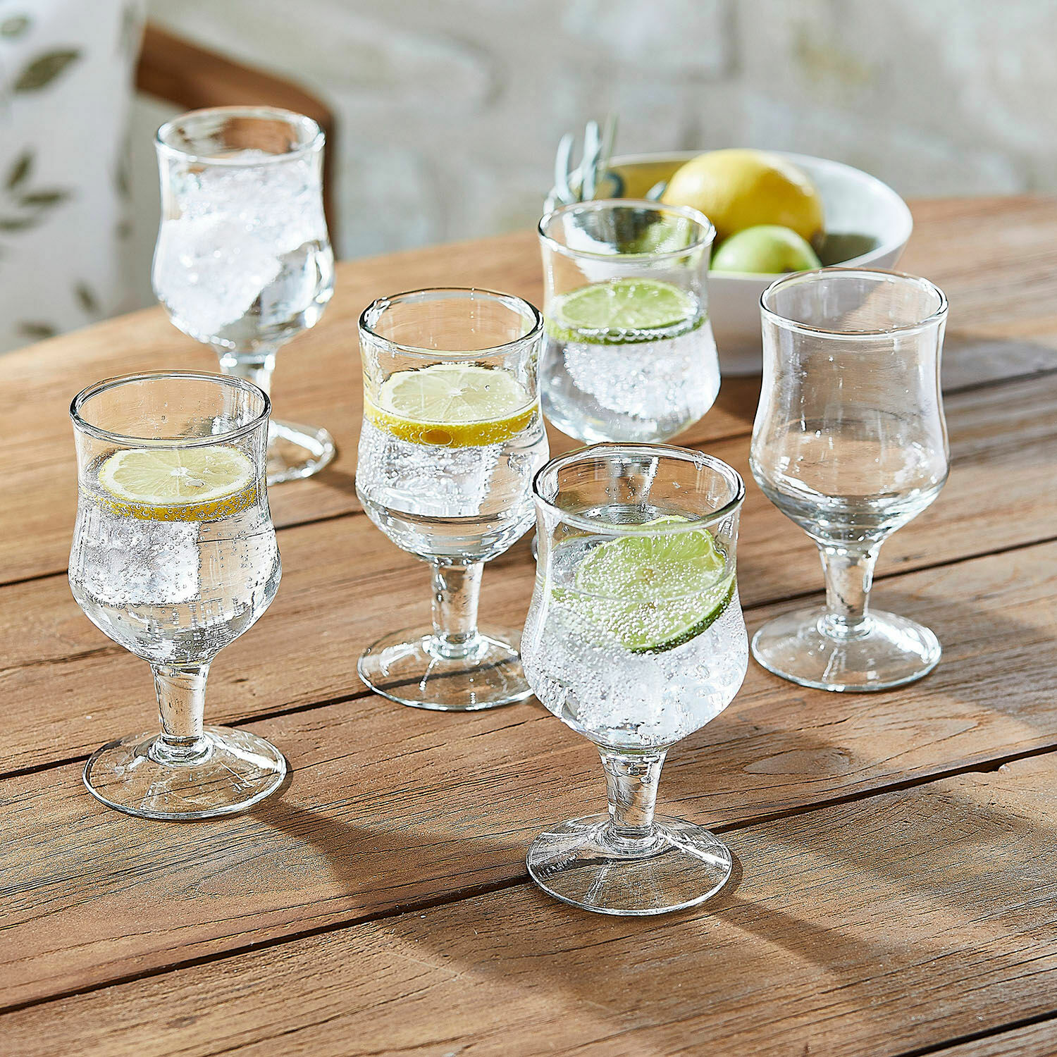 Lot de 6 verres Gaëtane Ensemble de six verres à pied en verre transparent avec tranches de citron et citron vert sur table en bois