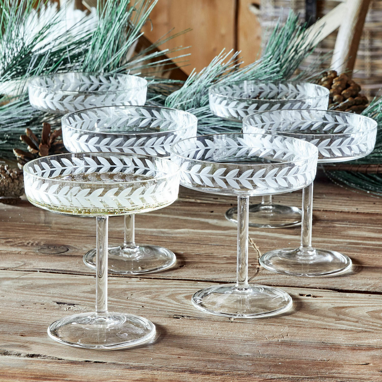 Lot de 6 coupes à champagne Macomb Ensemble de six coupes à champagne en verre avec motif gravé de feuilles sur une table en bois rustique