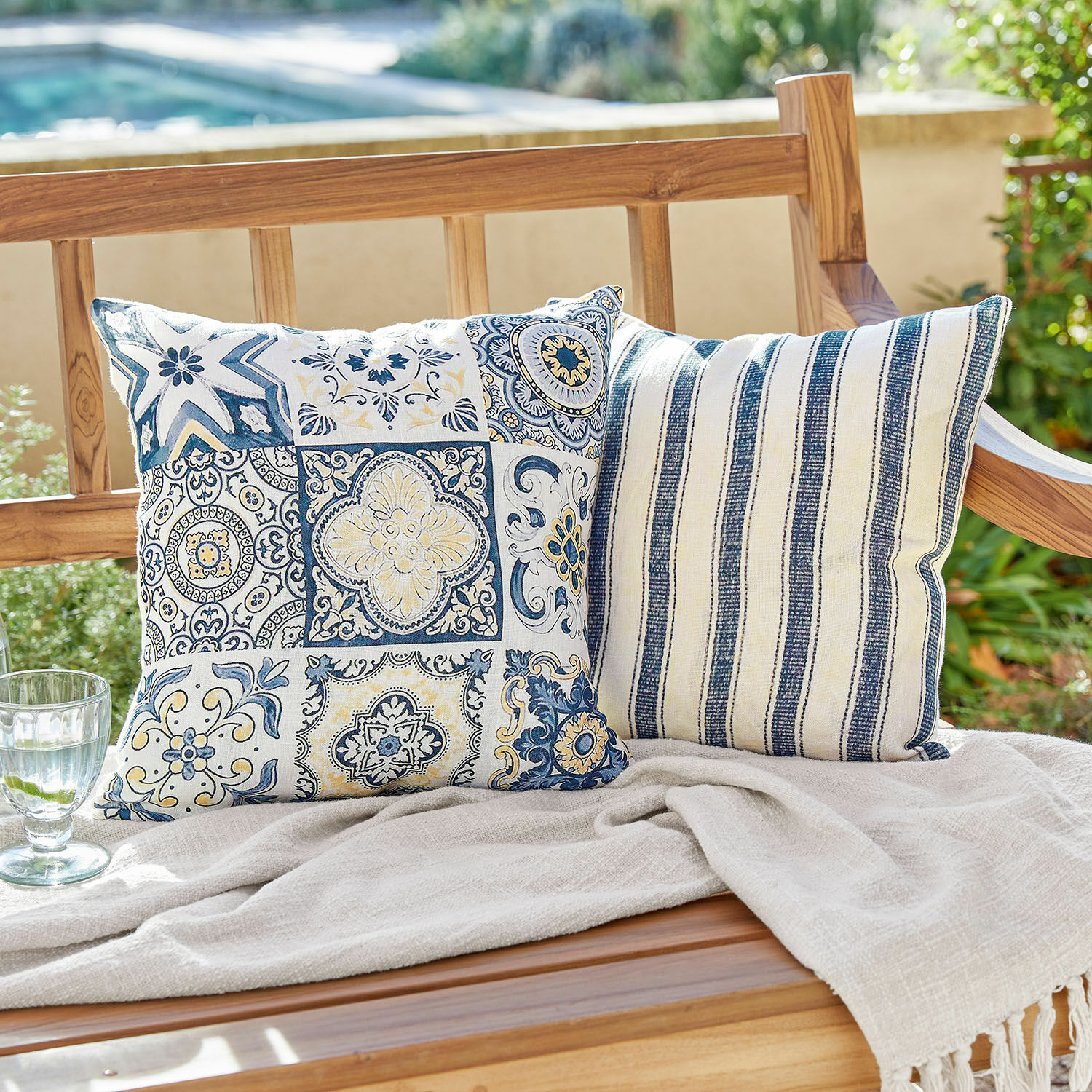 Lot de 2 housses de coussins Bourrignon Deux coussins décoratifs en coton bleu et blanc avec motifs sur un banc en bois dans un jardin