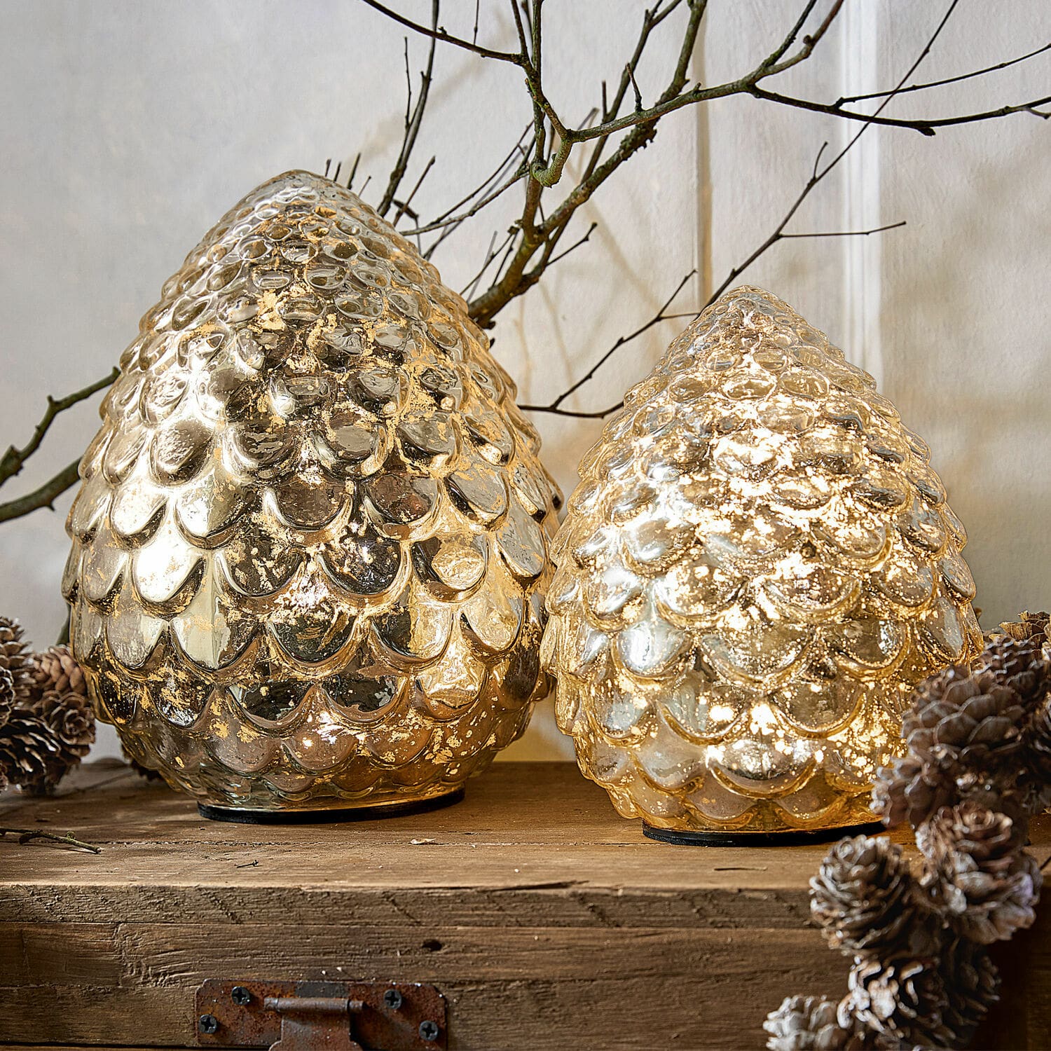 Lot de 2 pommes de pin à LED Ibaque Deux cônes décoratifs en verre doré avec texture écaille sur une surface en bois avec pommes de pin