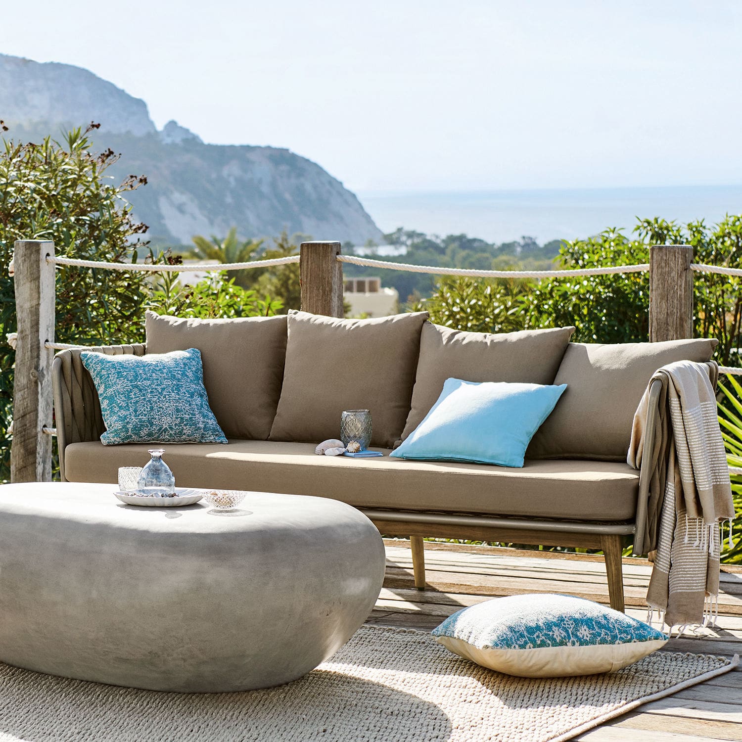 Canapé Siochana Canapé d'extérieur beige avec coussins bleus et table basse en pierre grise sur terrasse ensoleillée
