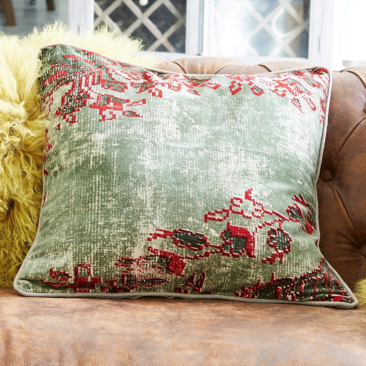 Coussin Vianney Coussin décoratif vert et rouge en tissu doux posé sur un canapé en cuir marron