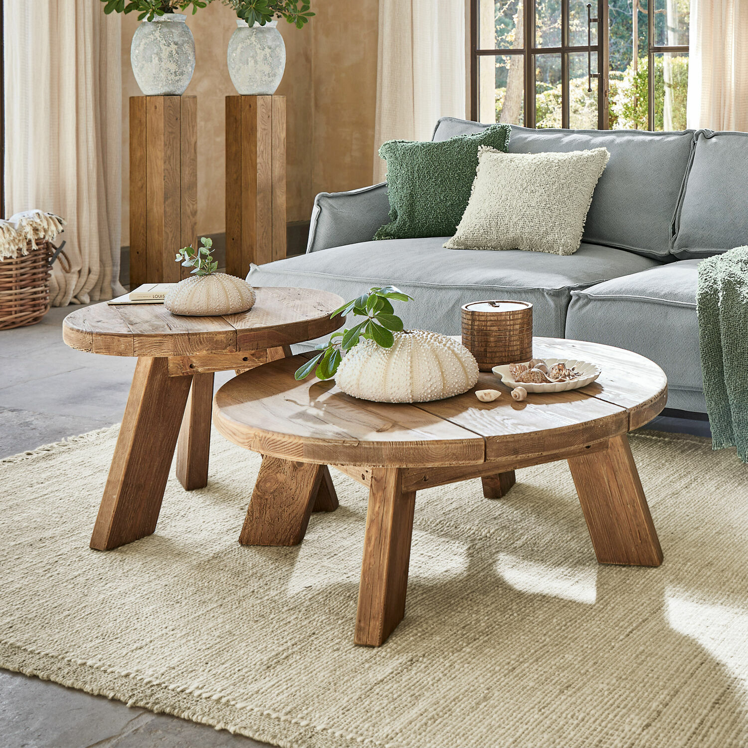 Lot de 2 tables d’appoint Oteley Deux tables basses rondes en bois naturel sur un tapis clair dans un salon avec un canapé gris