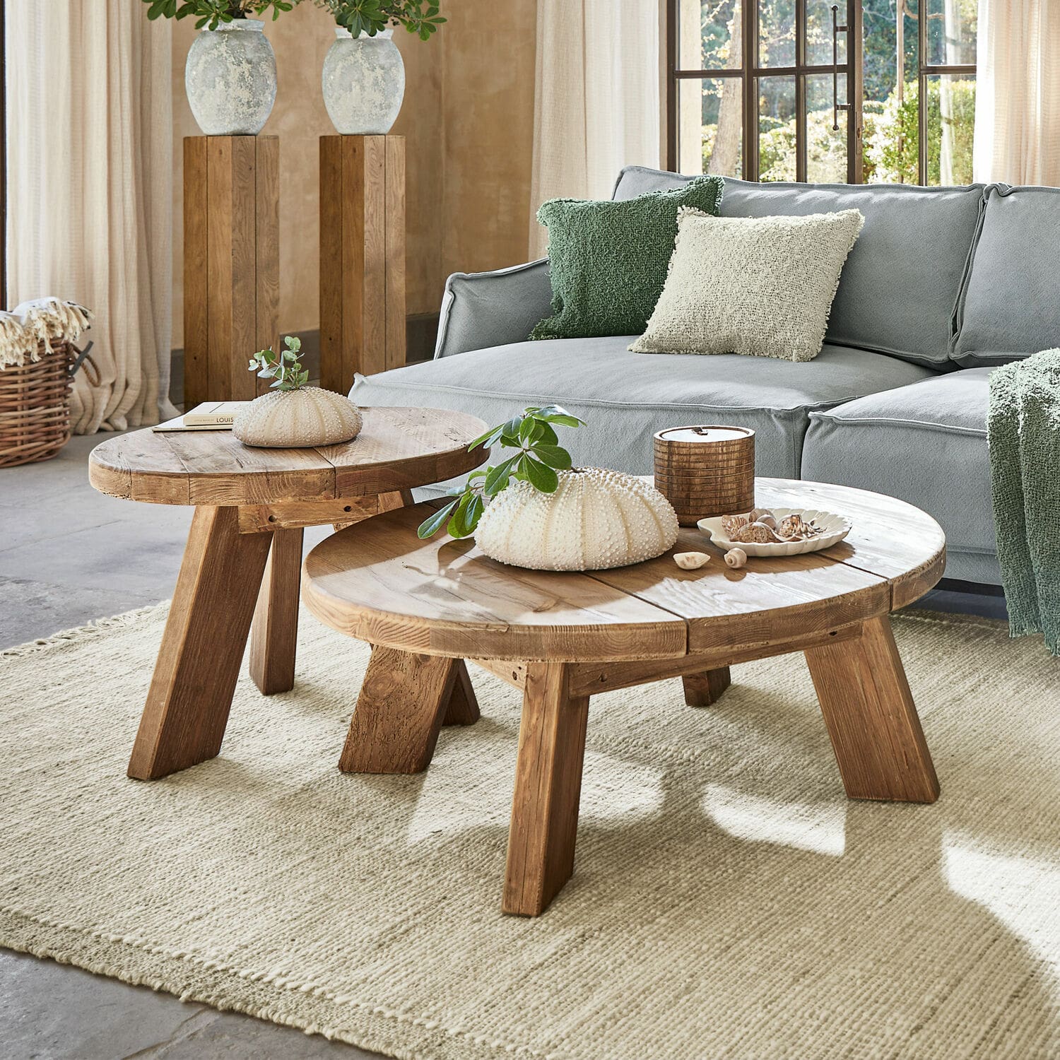 Lot de 2 tables d’appoint Oteley Deux tables basses rondes en bois naturel sur un tapis clair dans un salon avec un canapé gris