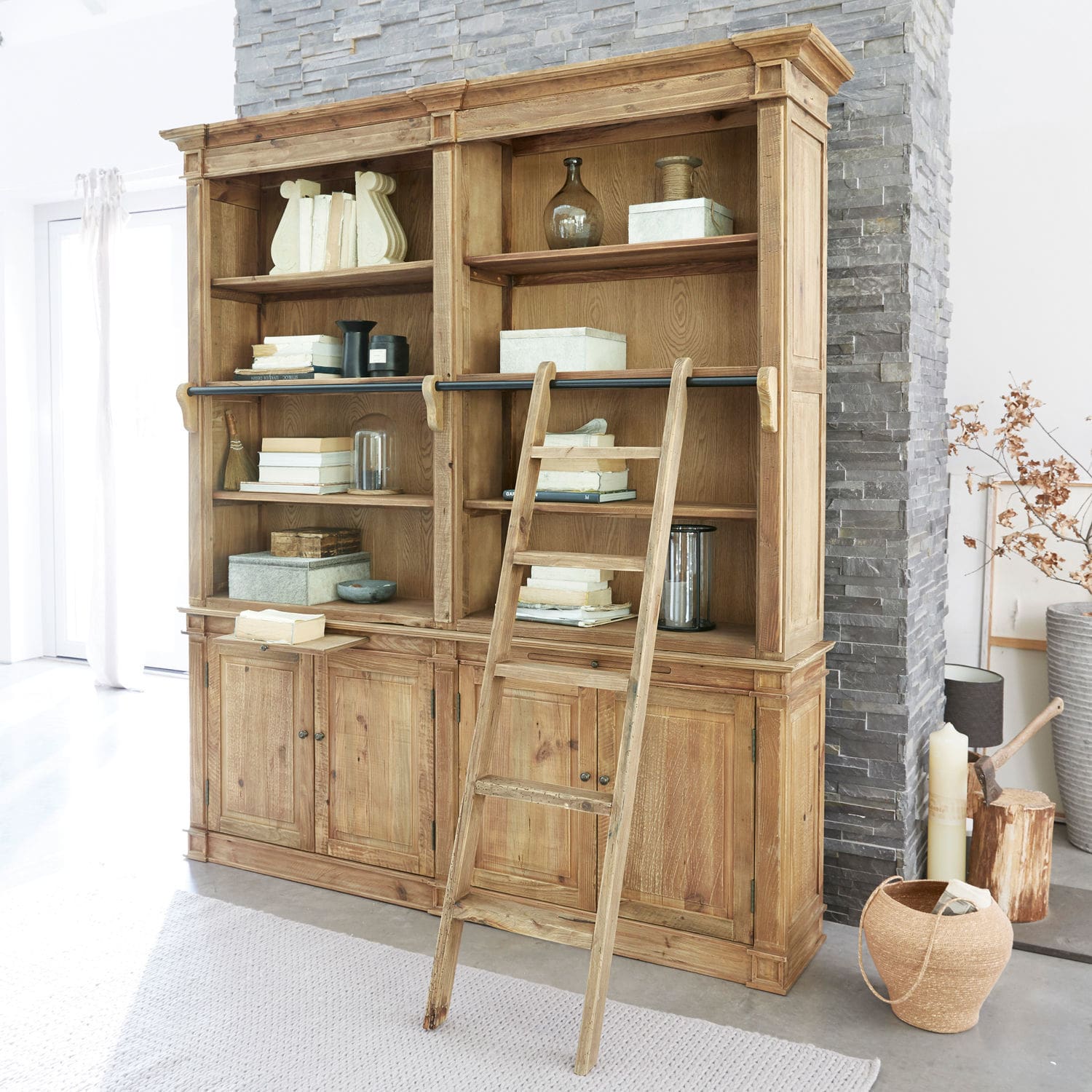 Buffet Livera Grande bibliothèque en bois avec échelle et étagères remplies de livres et décorations dans un intérieur lumineux