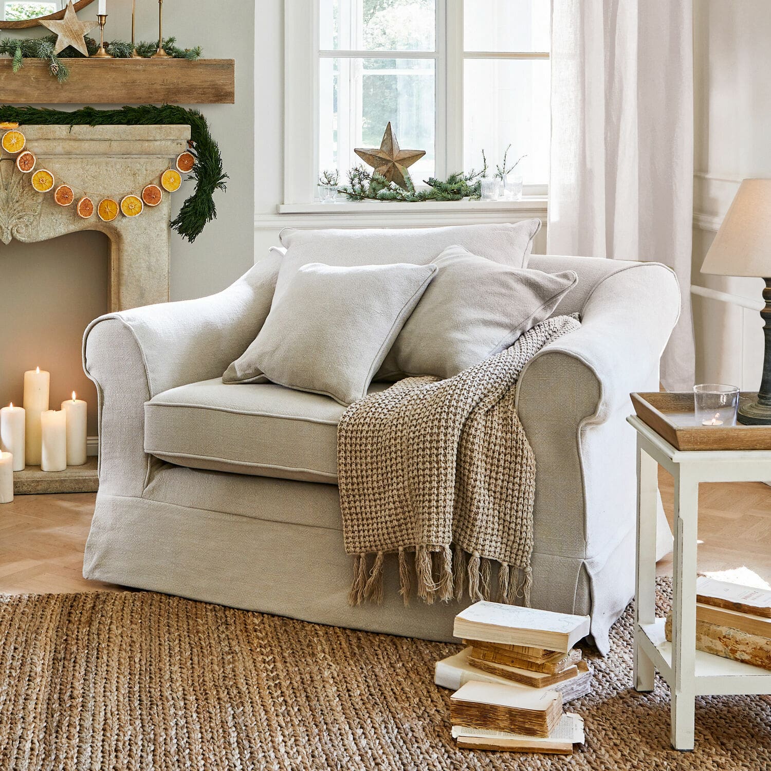 Fauteuil Folsom Canapé beige en tissu avec coussins et plaid tissé sur tapis en jute dans un salon chaleureux