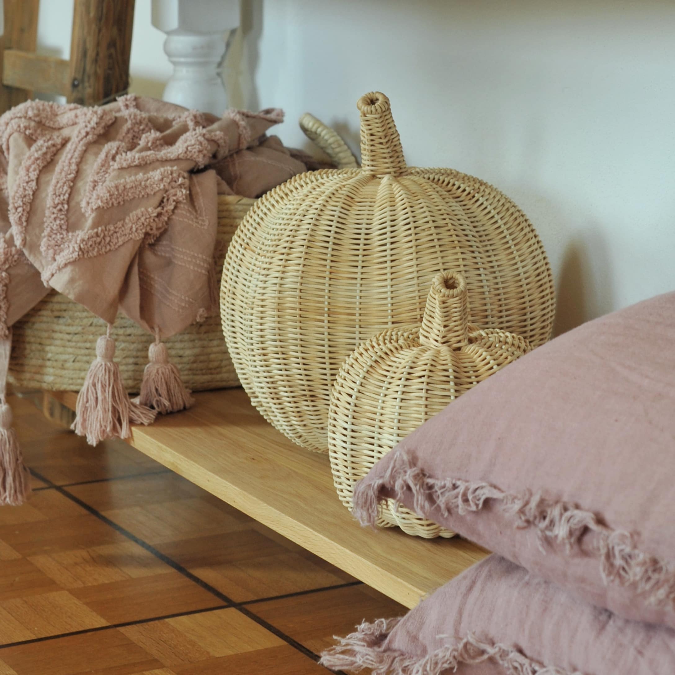 Citrouilles décoratives en rotin naturel sur une étagère en bois avec coussins roses