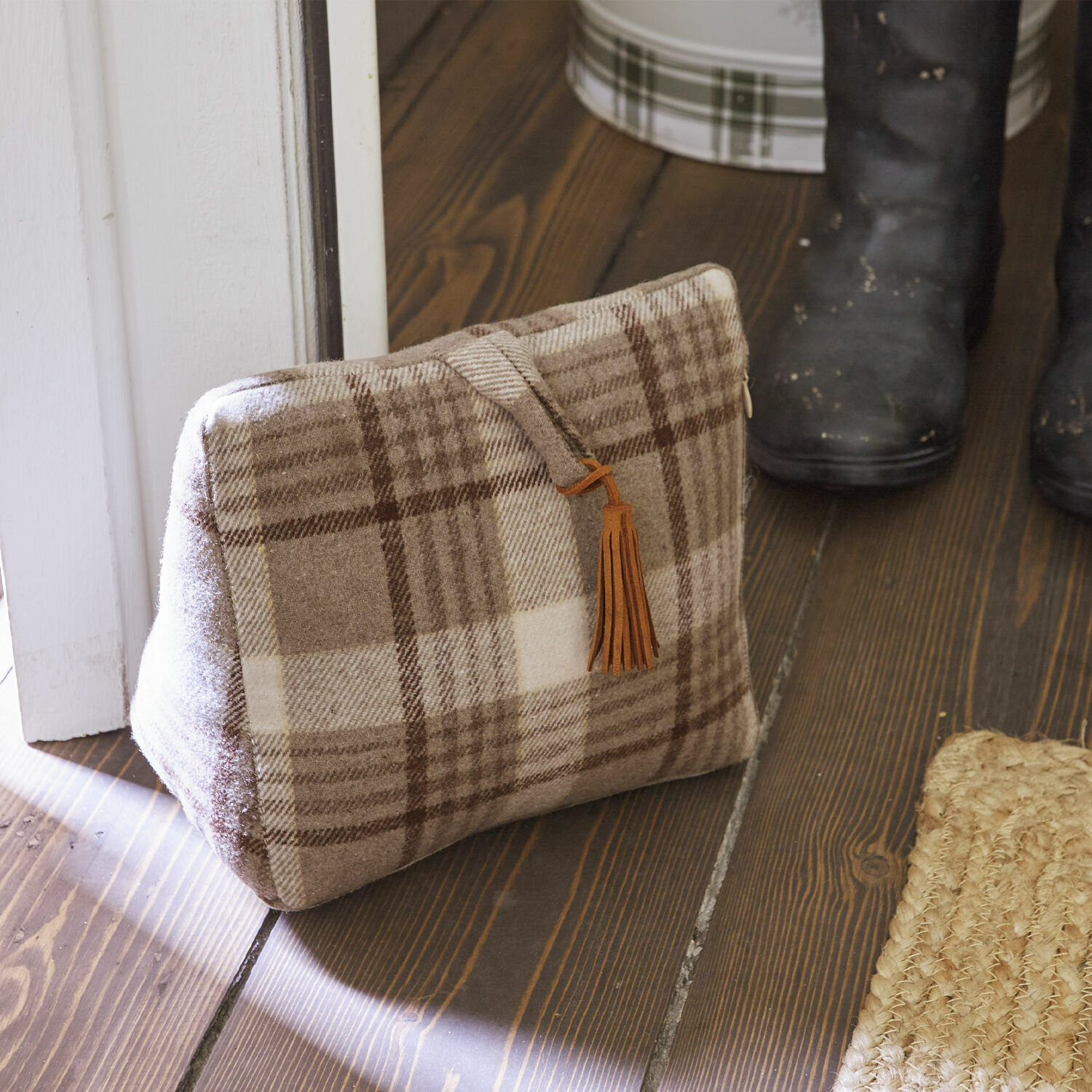 Bloque-porte Ersac Sac beige à carreaux en tissu doux avec pompon marron posé sur un sol en bois