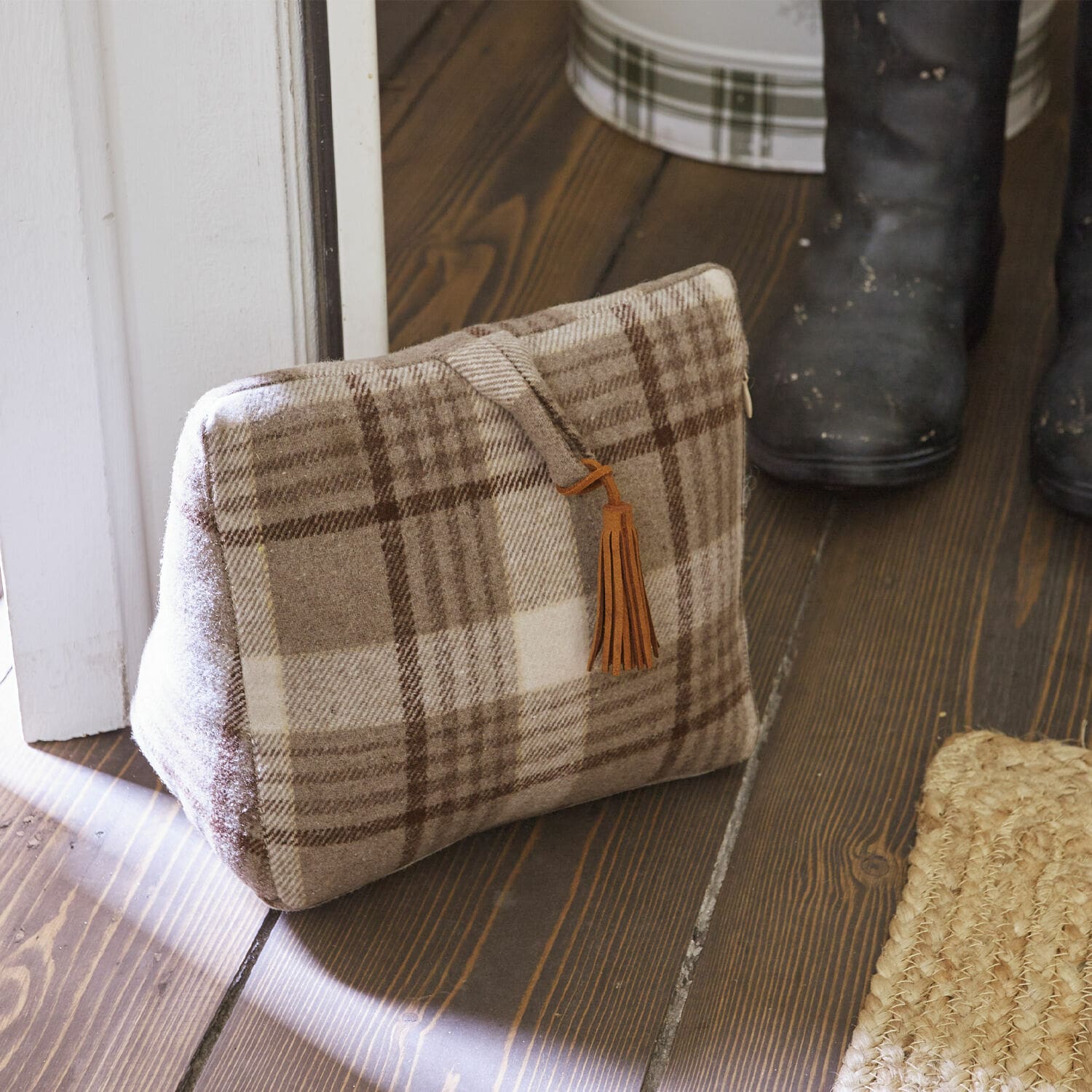 Bloque-porte Ersac Sac beige à carreaux en tissu doux avec pompon marron posé sur un sol en bois